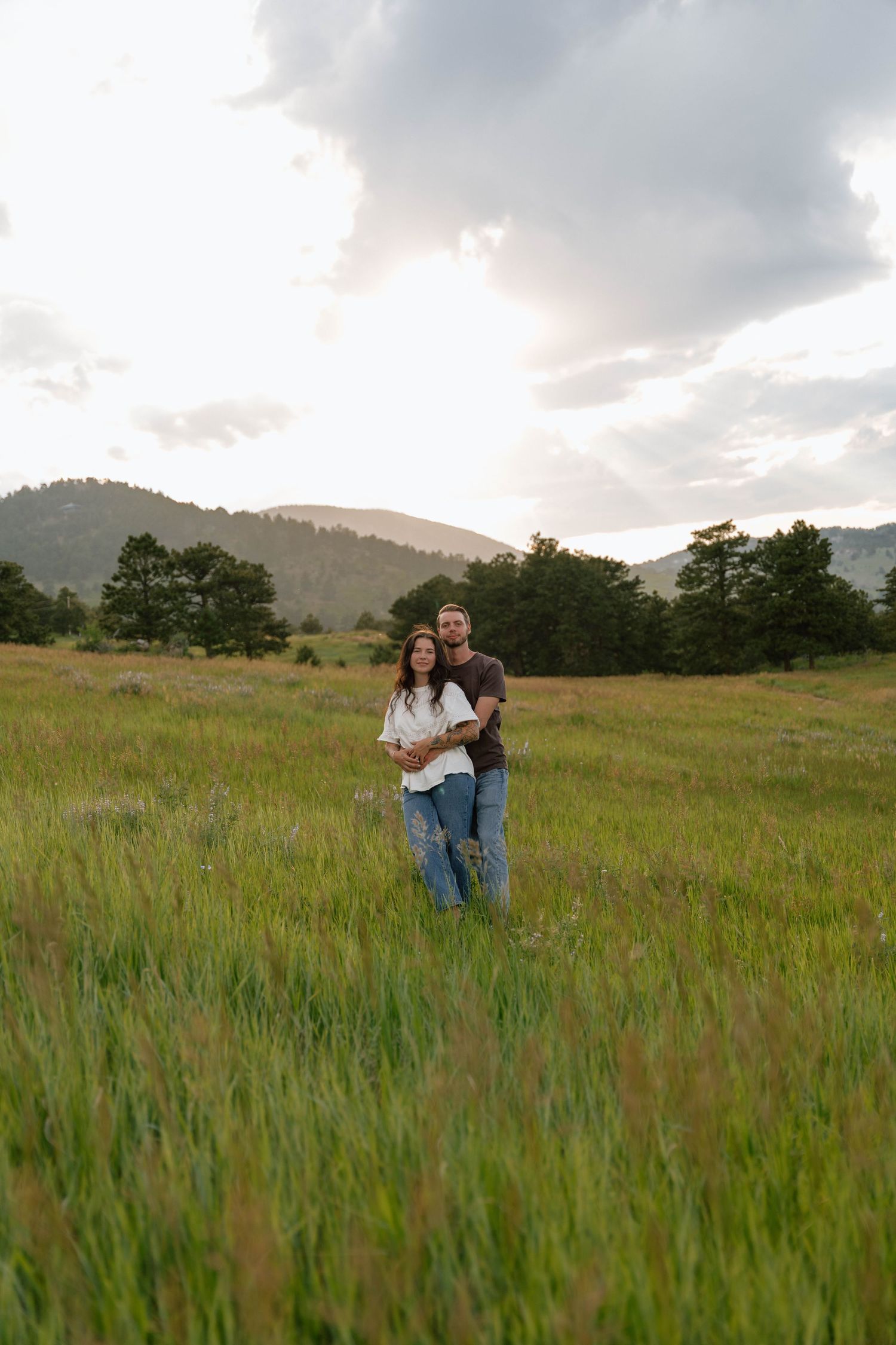A couple shares an intimate moment in a mountain meadow during golden hour.