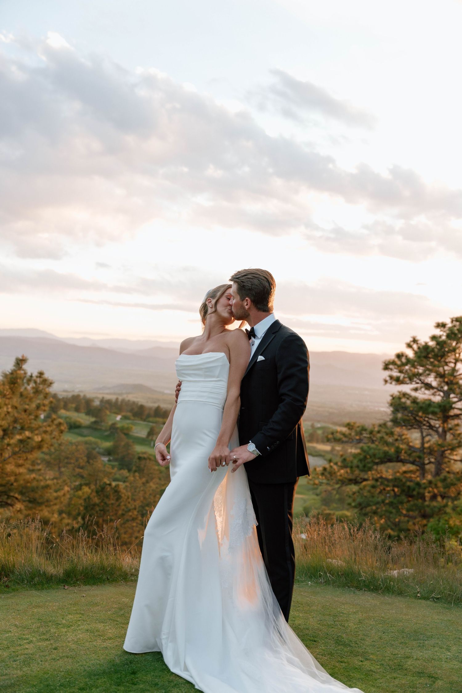 A couple shares their wedding day on a scenic hilltop with a dramatic sunset sky behind them.