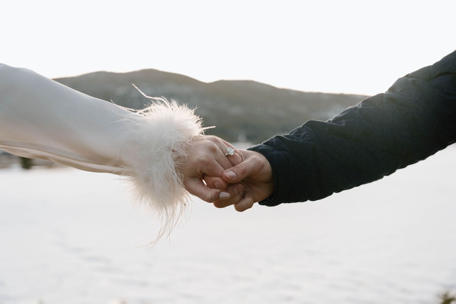 Close-up of hands reaching towards each other against a snowy mountain backdrop.