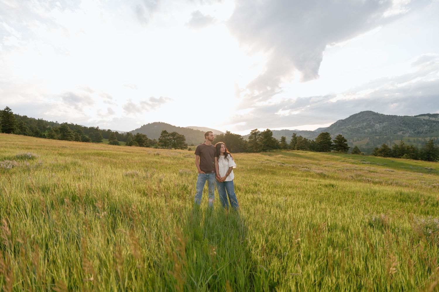 Wide landscape shot of a grassy field with mountains and two distant figures.