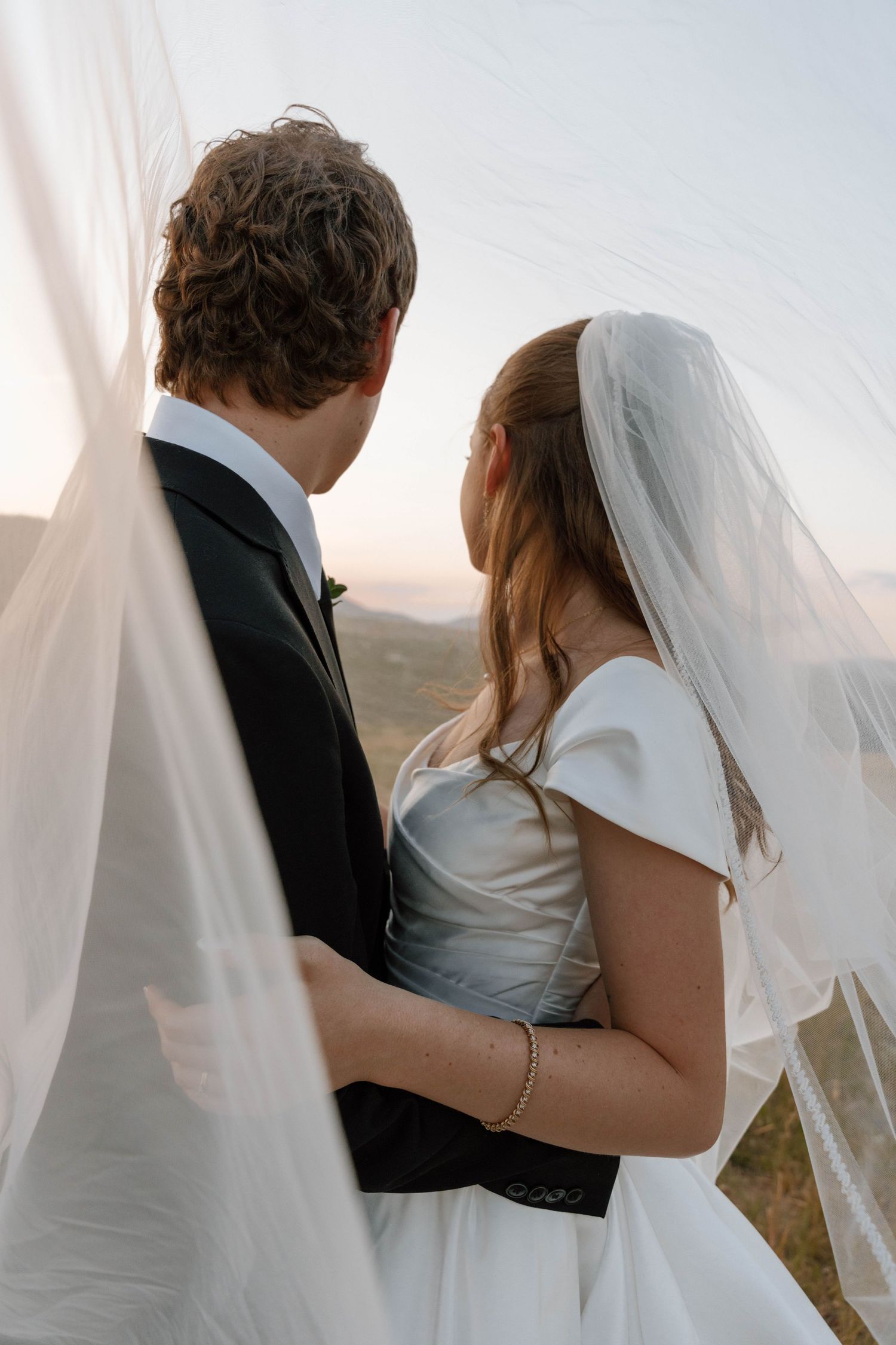 Romantic silhouette of couple against sunset with flowing veil in mountain landscape.