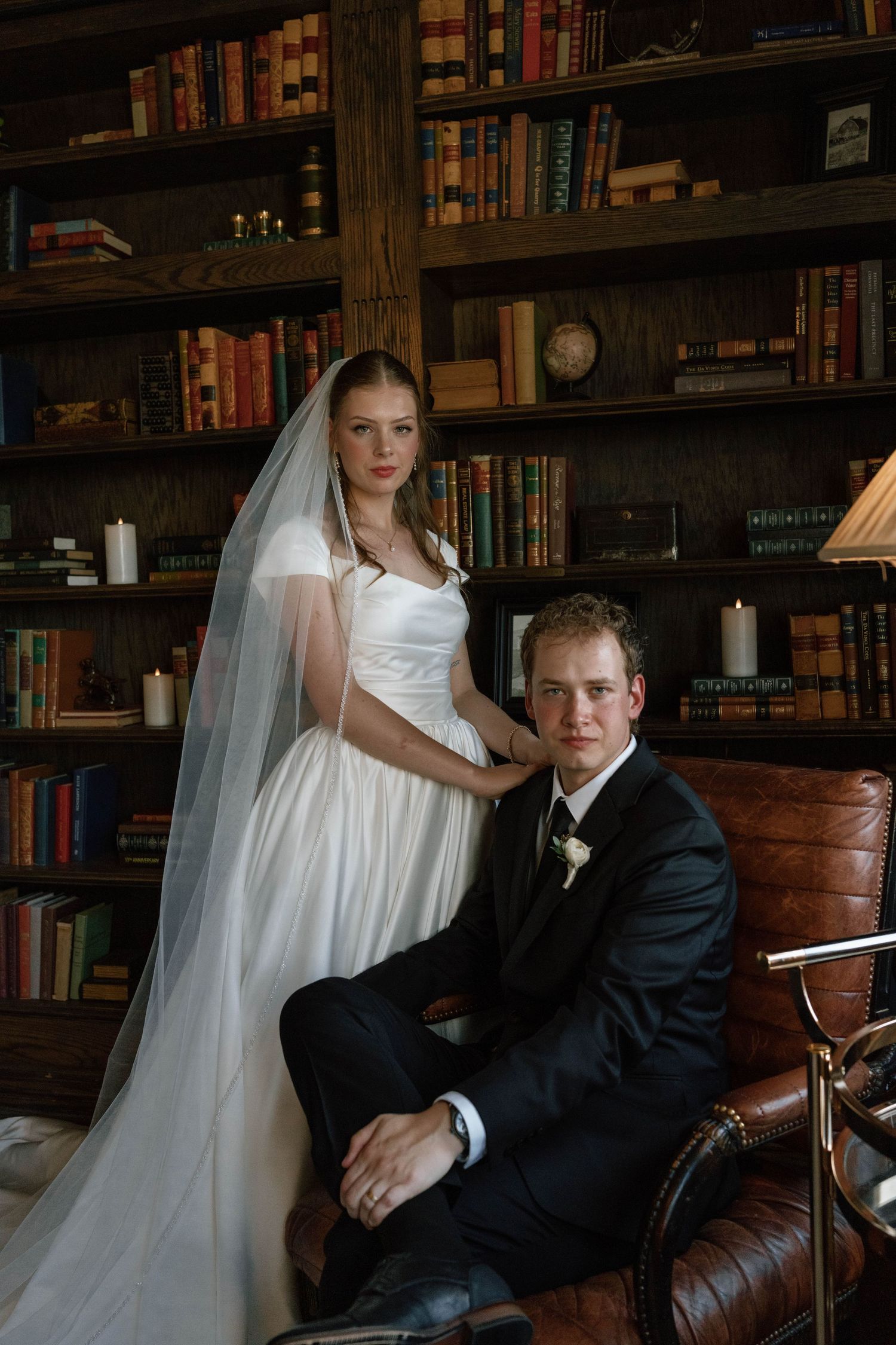 Wedding portrait session in vintage library with leather chair and wall-to-wall bookshelves.