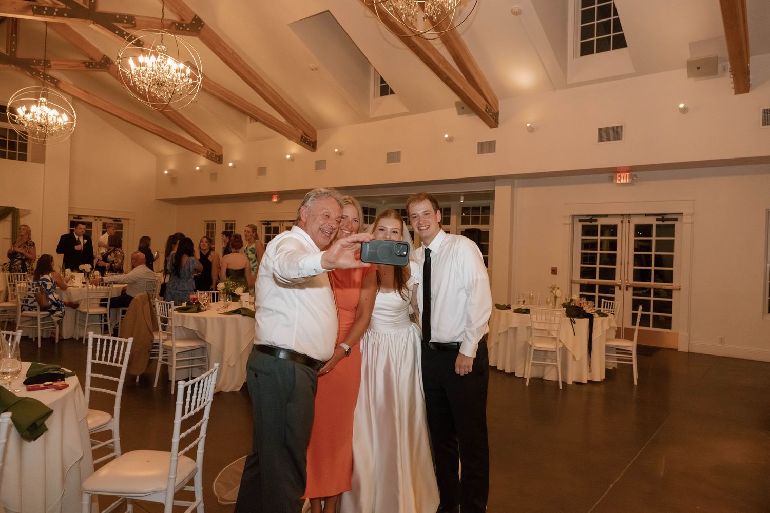 Wedding guests dancing and celebrating in an elegant reception venue with exposed wooden beams and chandeliers.