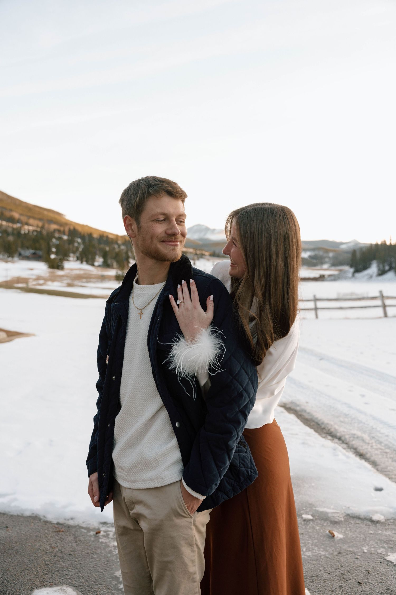 A romantic winter engagement photoshoot with a couple embracing against a snowy mountain backdrop.