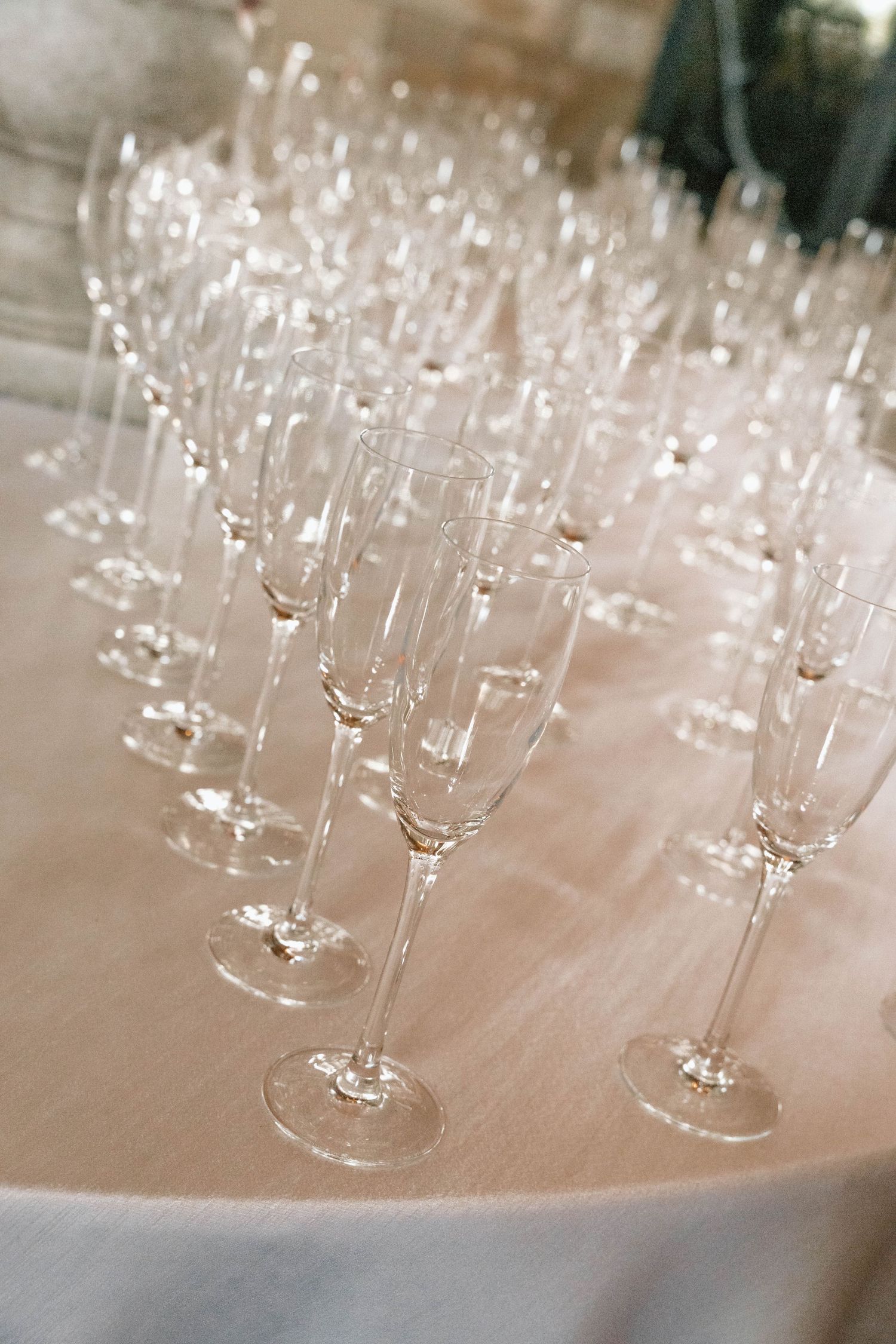Rows of empty champagne flutes arranged on white tablecloth.
