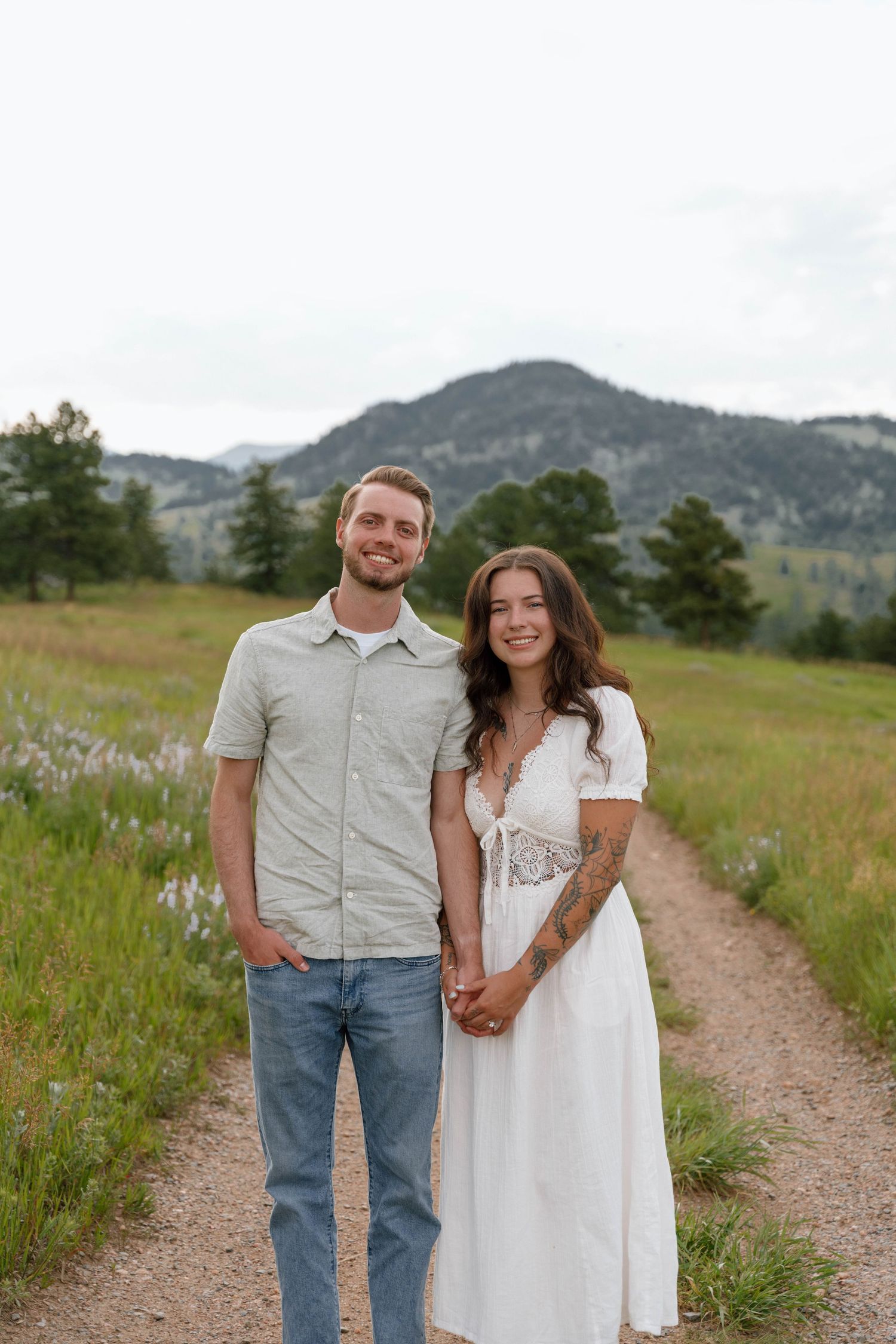 Couple standing on dirt path with mountain vista in background.