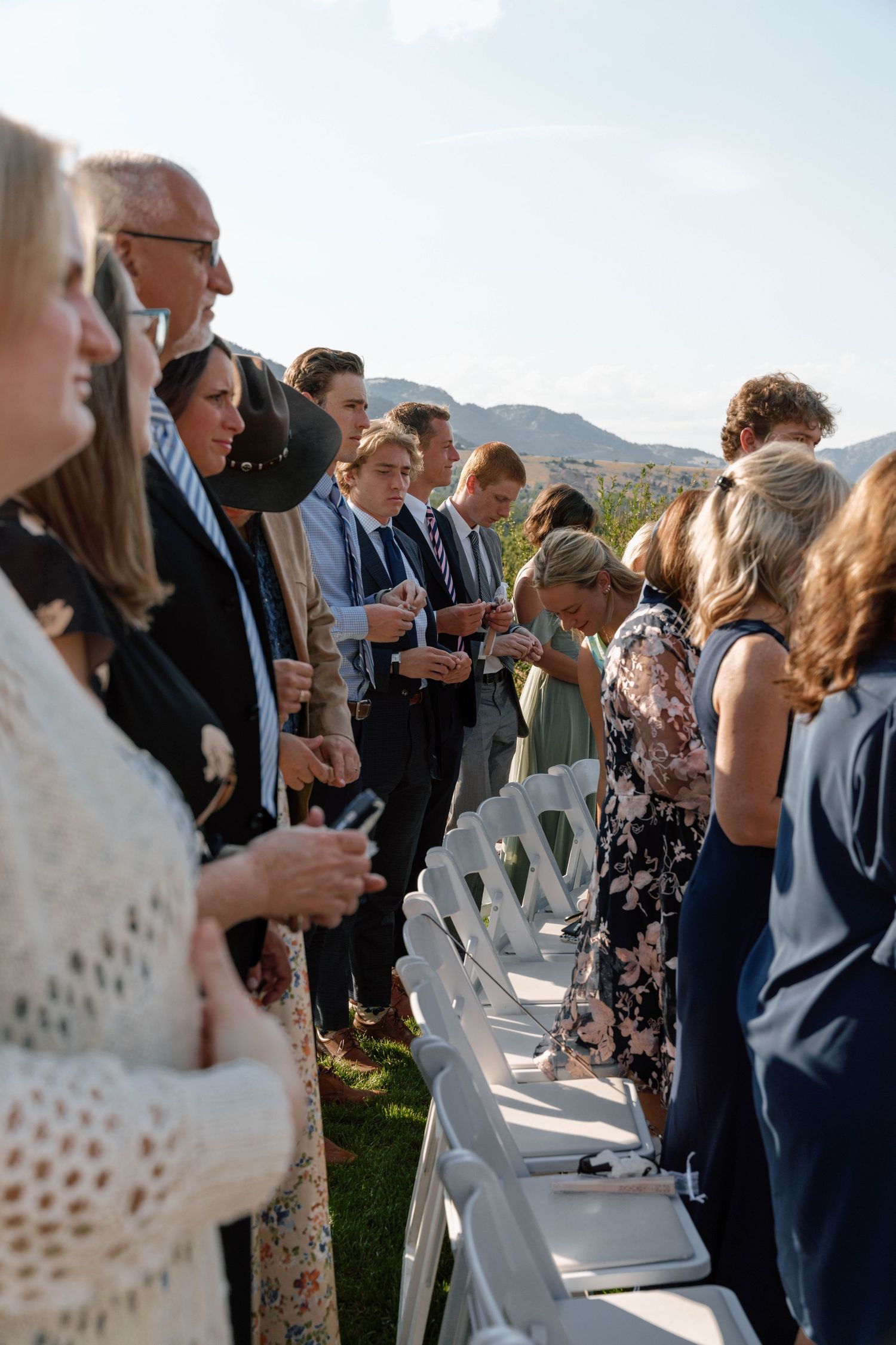 Wedding guests mingling and standing by white chairs during an outdoor reception.