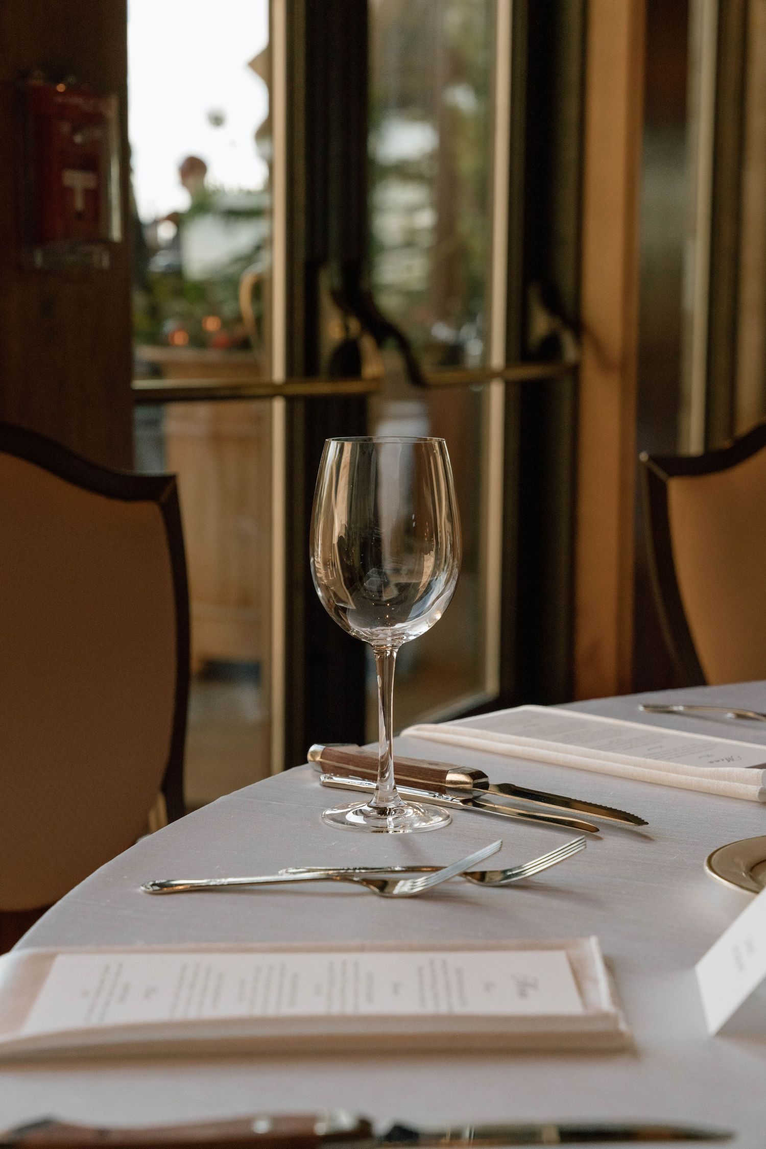 Elegant table setting at upscale restaurant with white tablecloth, wine glass, and formal place settings.