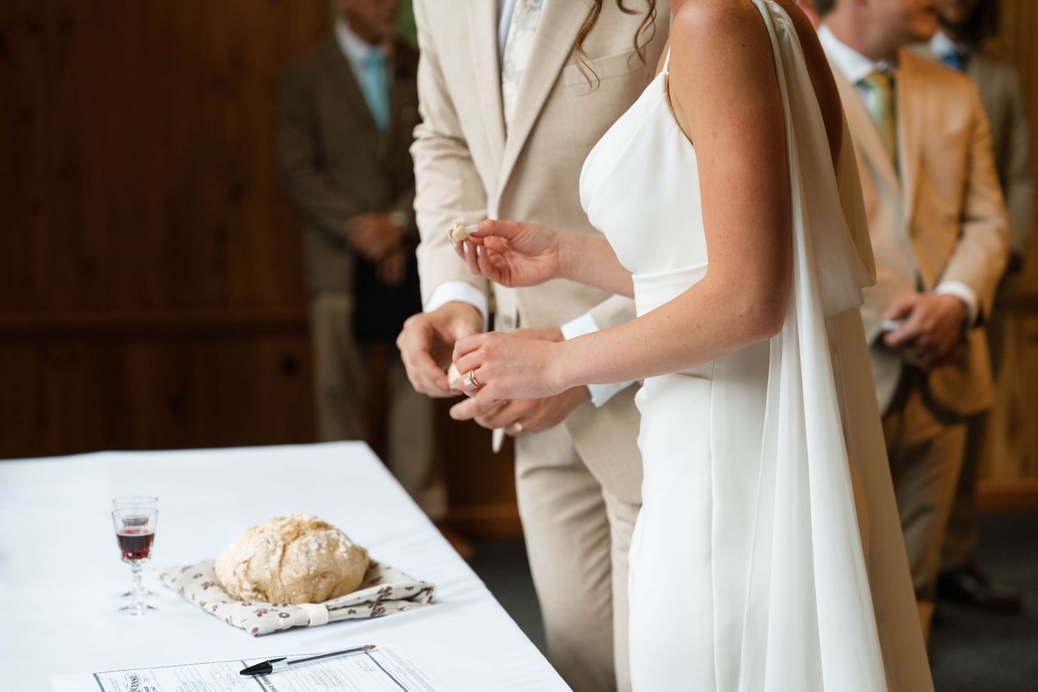 Bride and groom cutting bread at wedding ceremony altar with wine glass on white tablecloth.