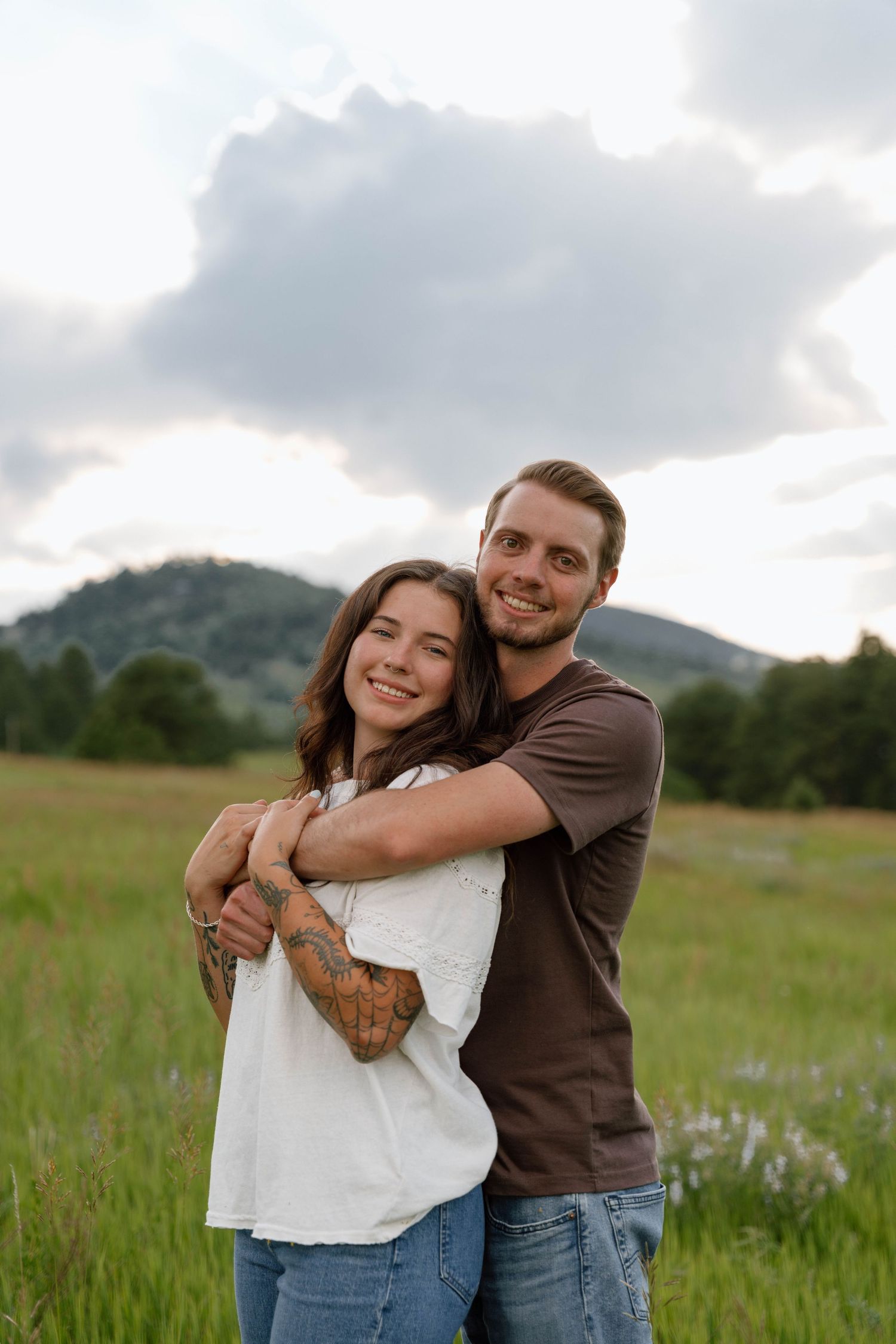 Happy couple hugging and laughing together in a mountain meadow at sunset.