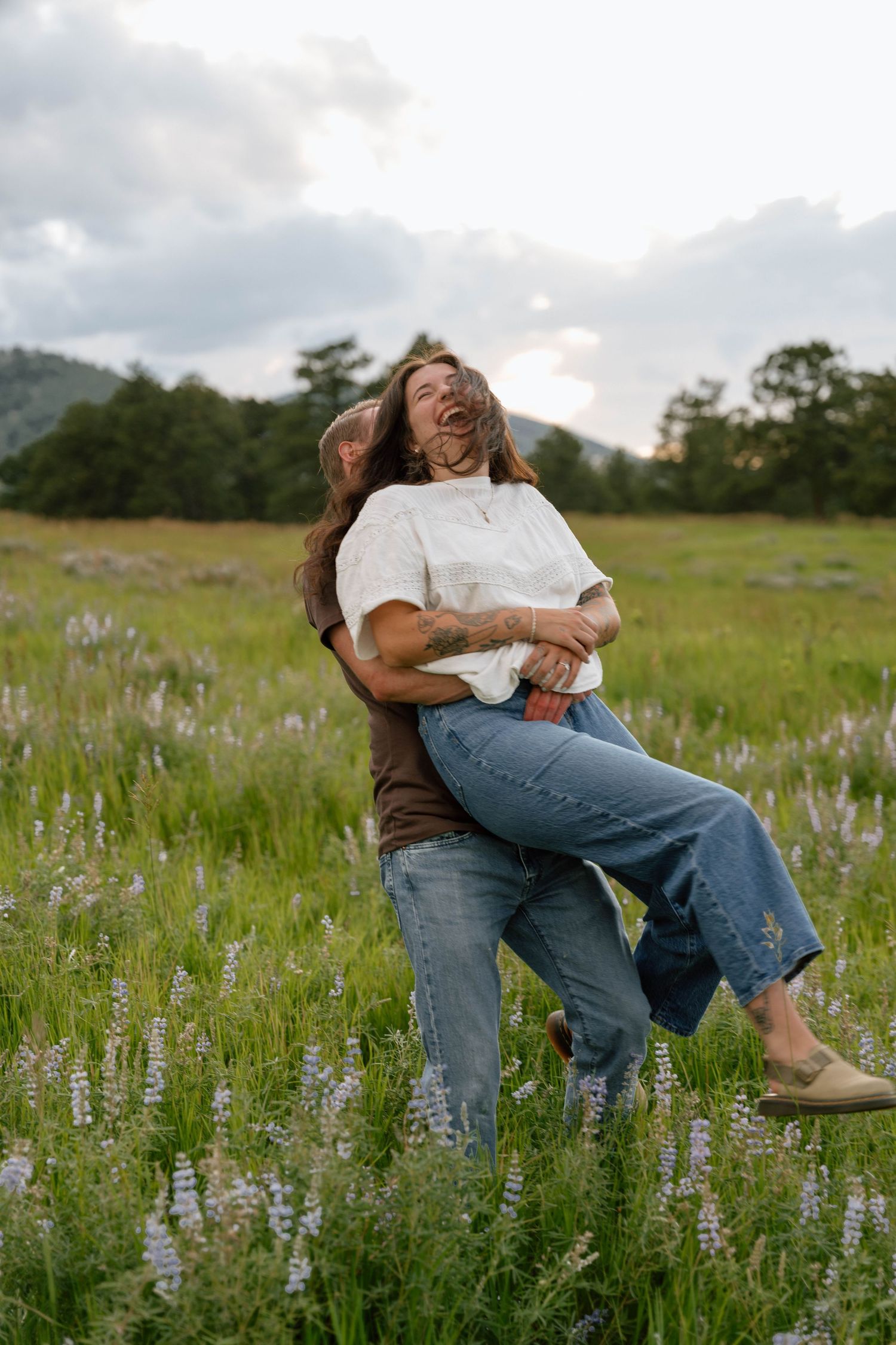 Couple sharing playful moments among purple wildflowers in a mountain meadow.