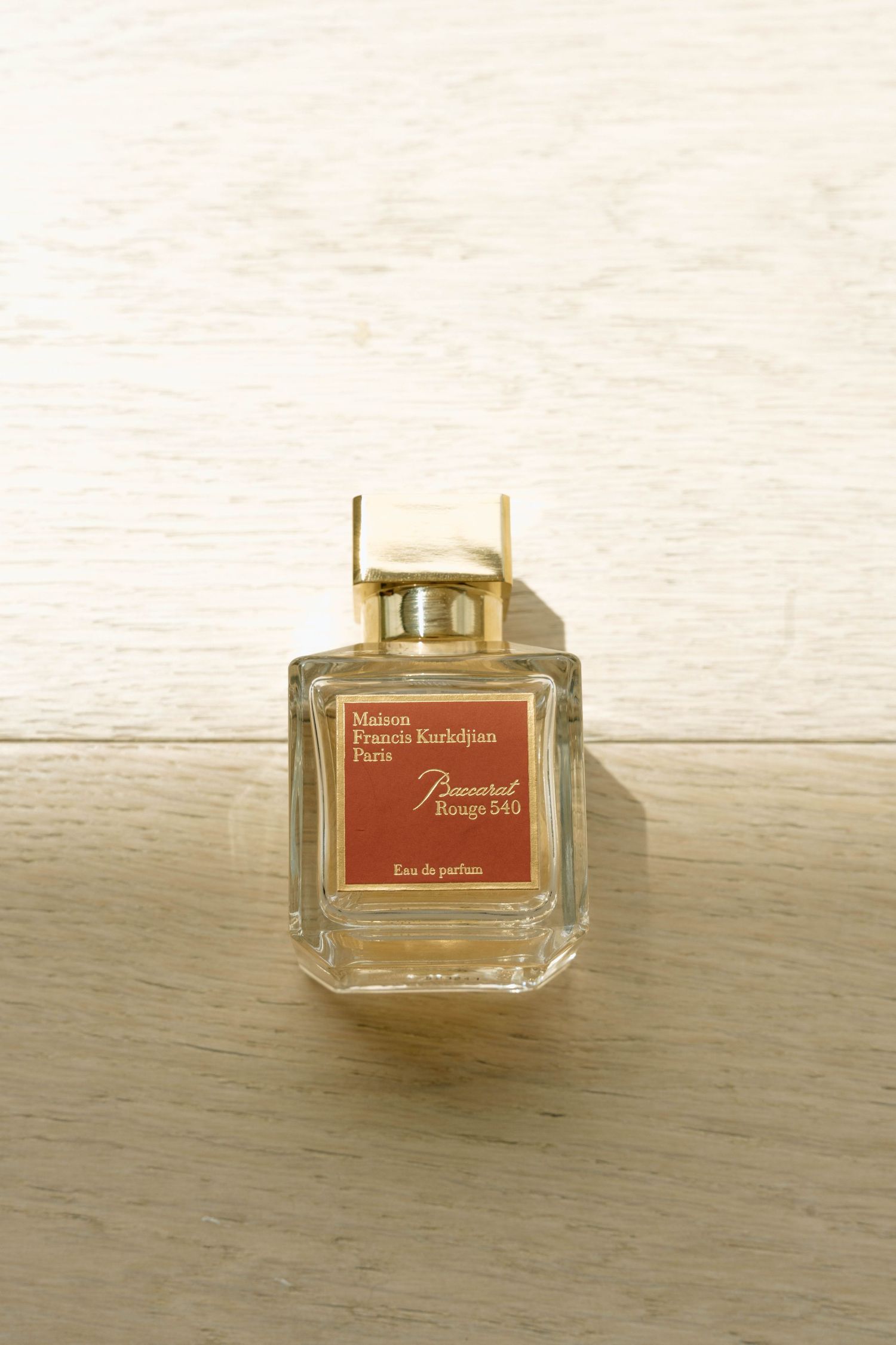 A bottle of Baccarat Rouge 540 perfume sitting on a light wooden surface.
