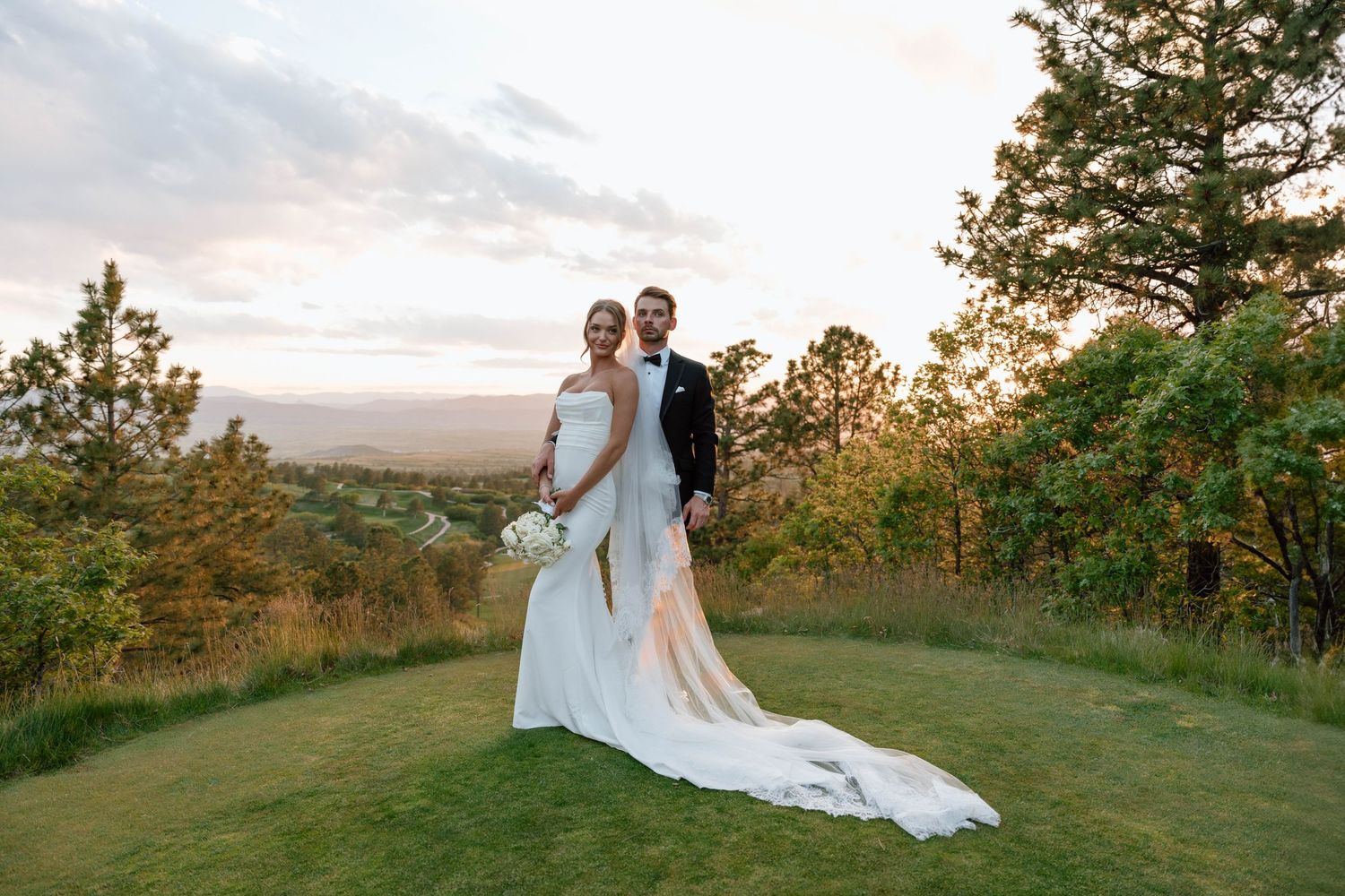 Romantic sunset wedding photos captured on a hilltop surrounded by trees.