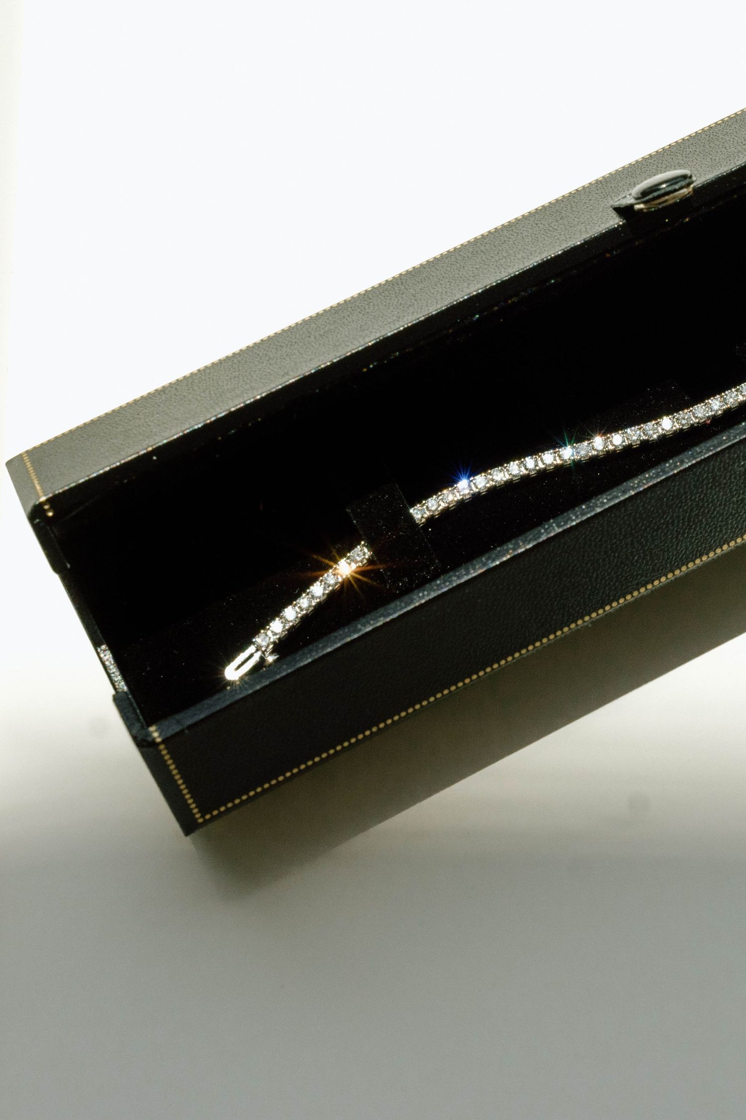 Diamond tennis bracelet displayed in an open black velvet jewelry box with gold trim detailing.
