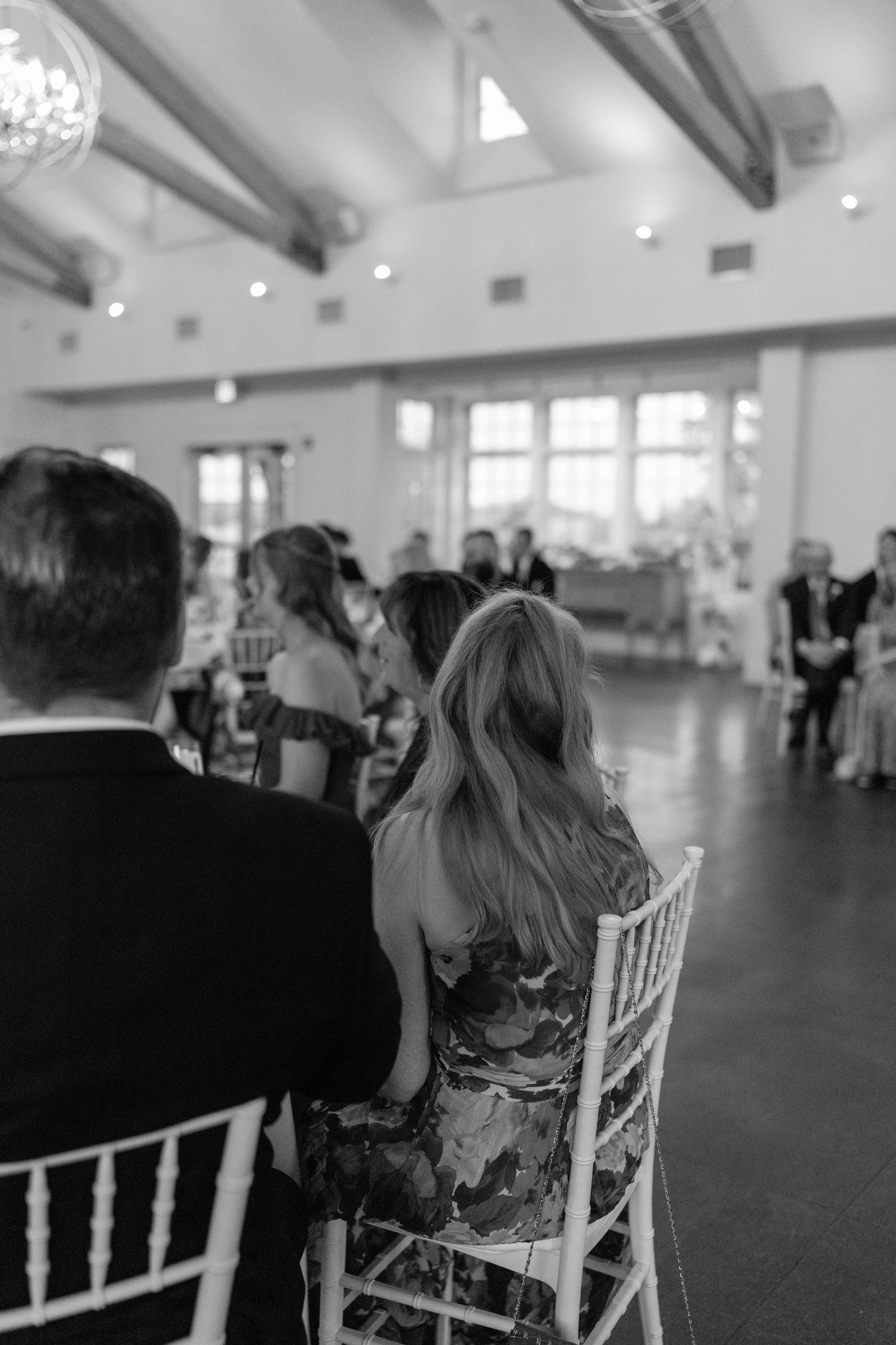 Wedding guests seated in white chairs during an indoor reception.