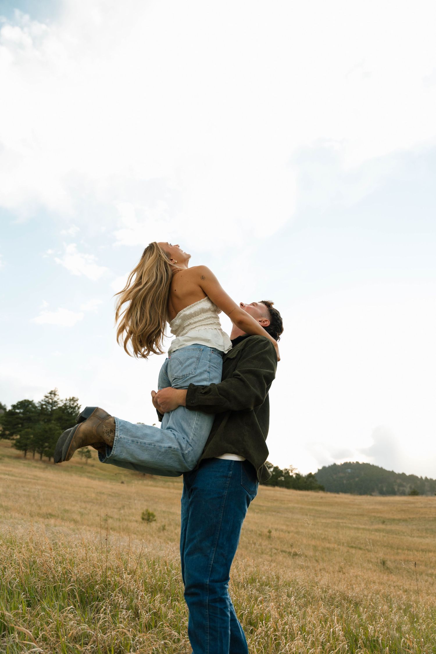 A joyful couple in a golden field, man lifting laughing woman into the air, sharing a romantic moment outdoors.