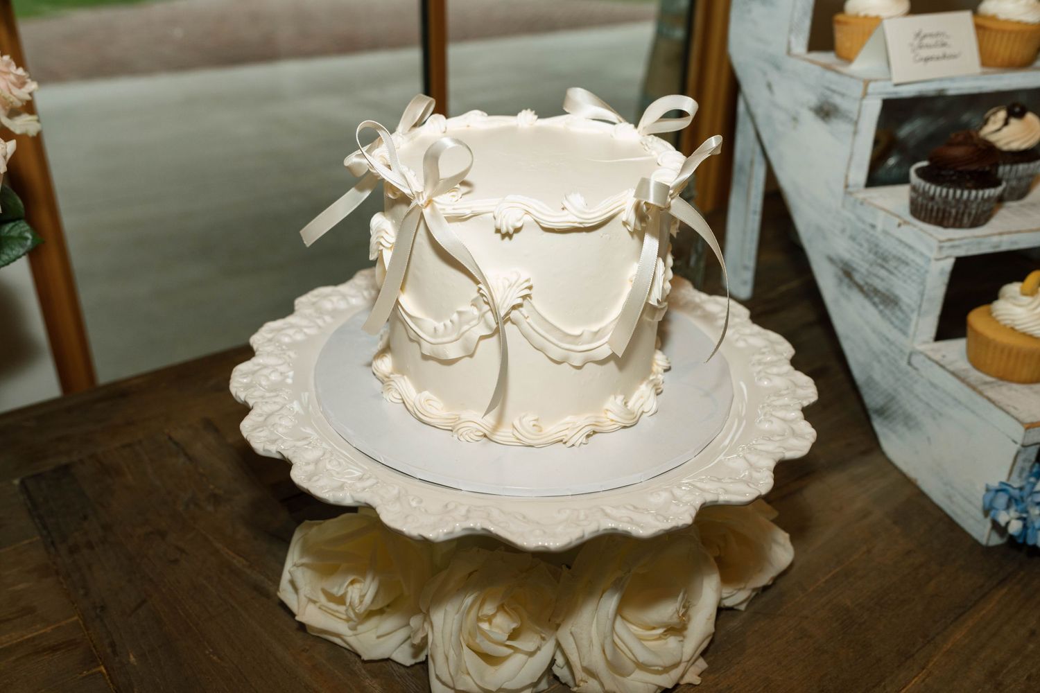 Elegant white fondant wedding cake with bow and swag details on decorative stand.