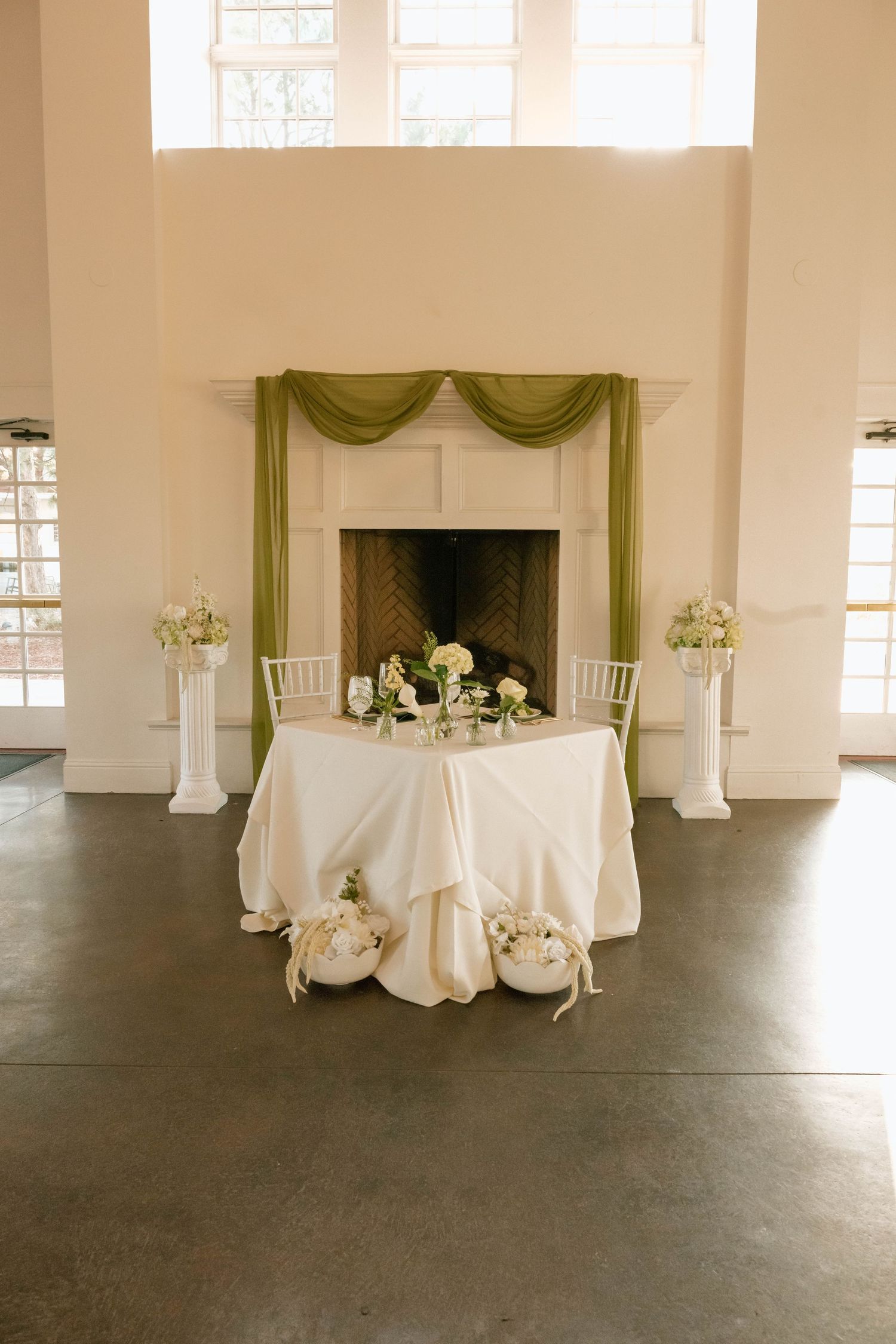 Wedding reception hall with white tablecloths and green drapery accents.