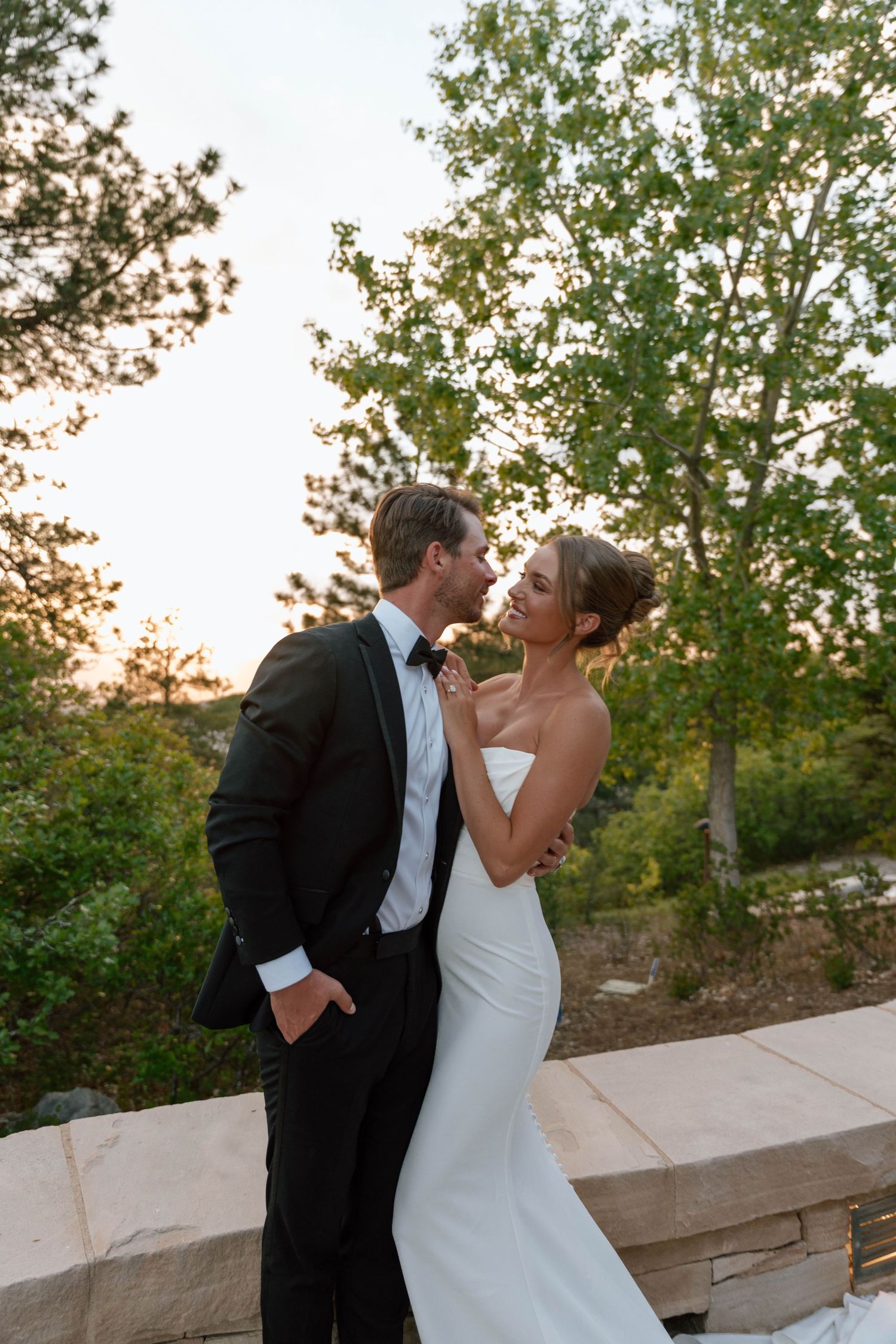 A romantic sunset wedding photo with couple sharing a tender moment against green foliage.