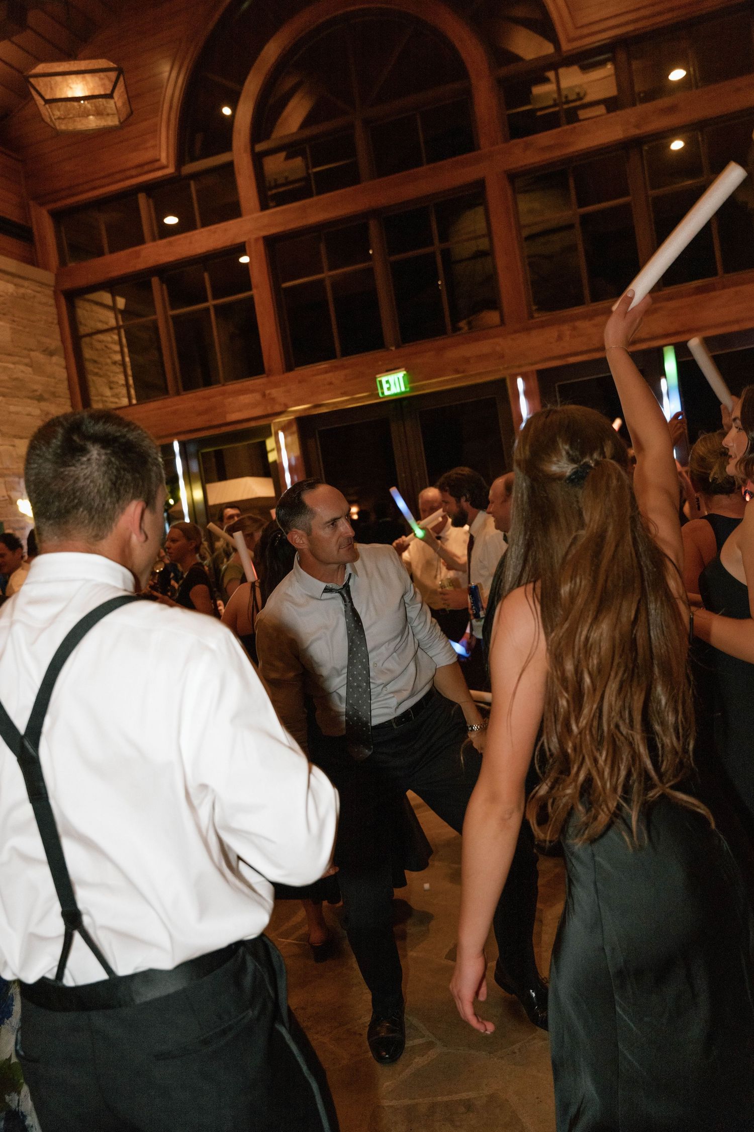 Wedding reception guests dancing energetically under warm lighting and wooden beams.