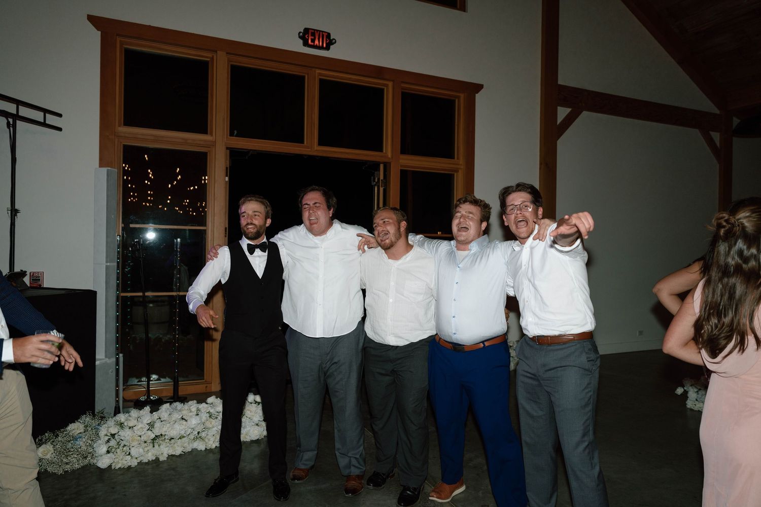 Groom celebrating with groomsmen and friends on dance floor at rustic barn wedding reception.