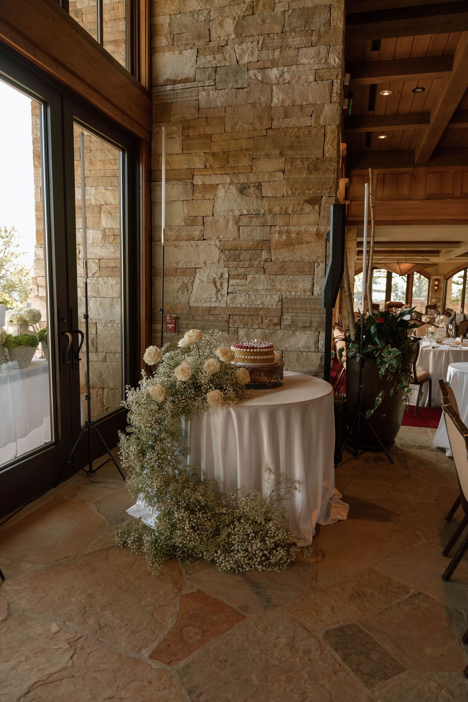 An elegant wedding reception space with stone walls, white linens, and natural light streaming through windows.