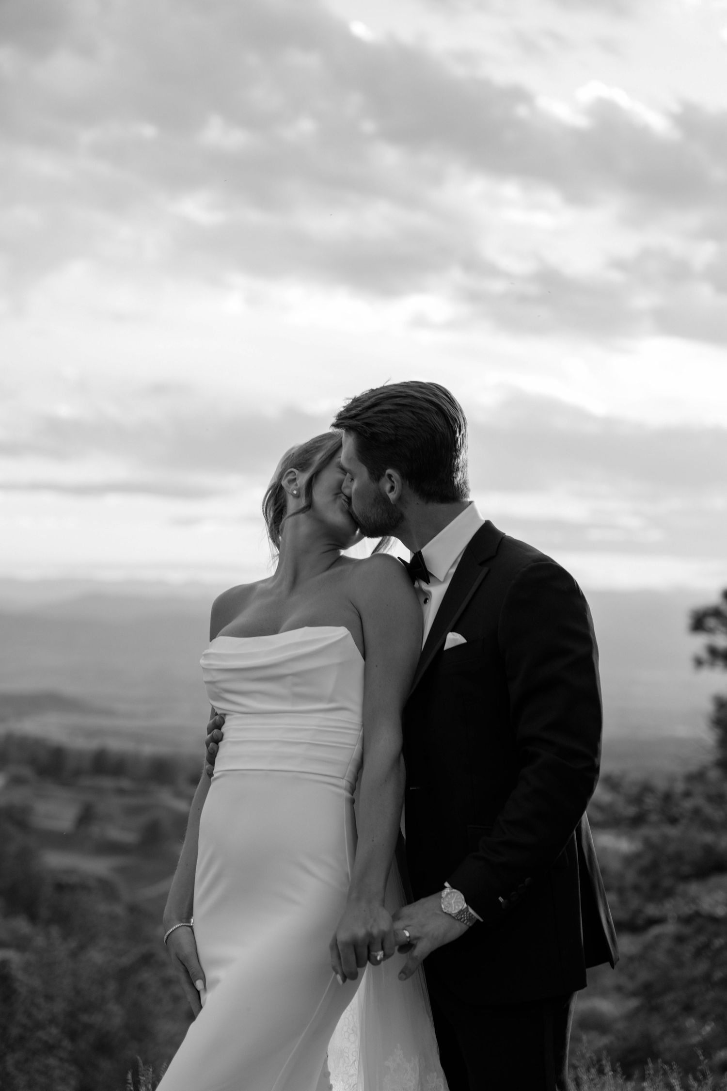 Black and white wedding portrait captures an intimate moment between newlyweds on a hillside.