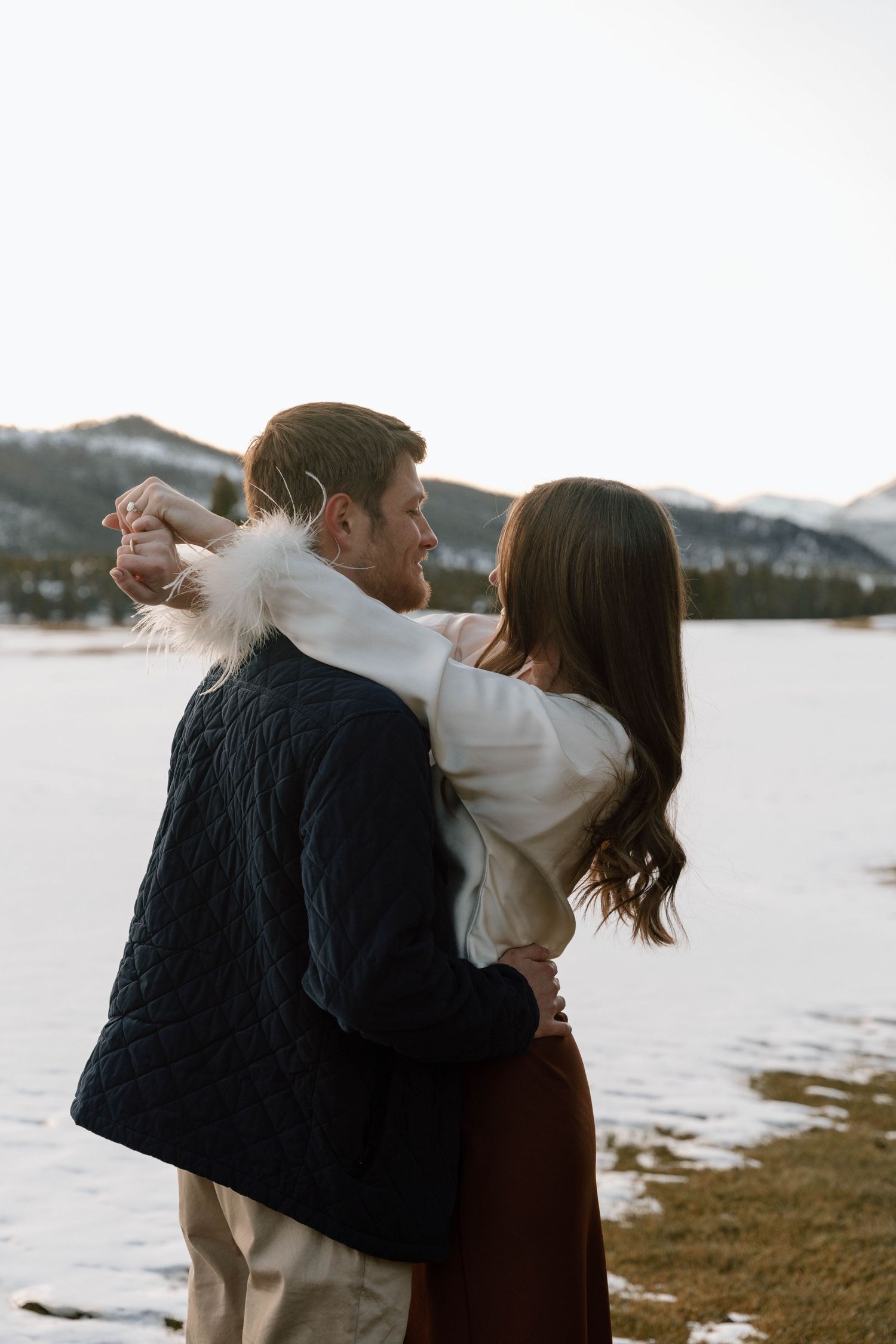 Playful engagement photos of a couple dancing and spinning in a snowy mountain setting.