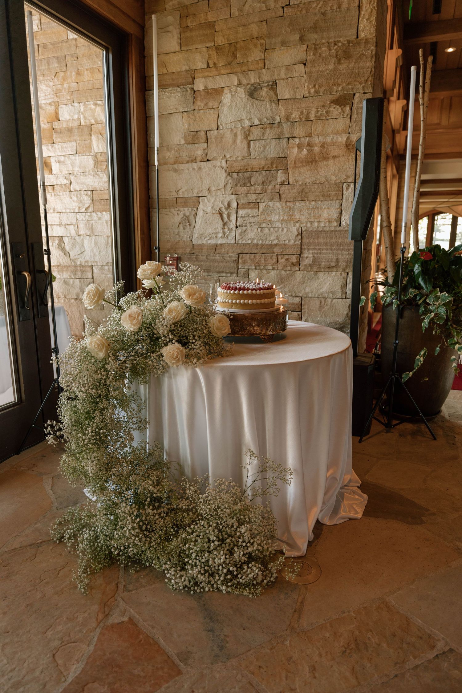Round reception tables with white linens and baby's breath floral arrangements in a stone-walled venue.