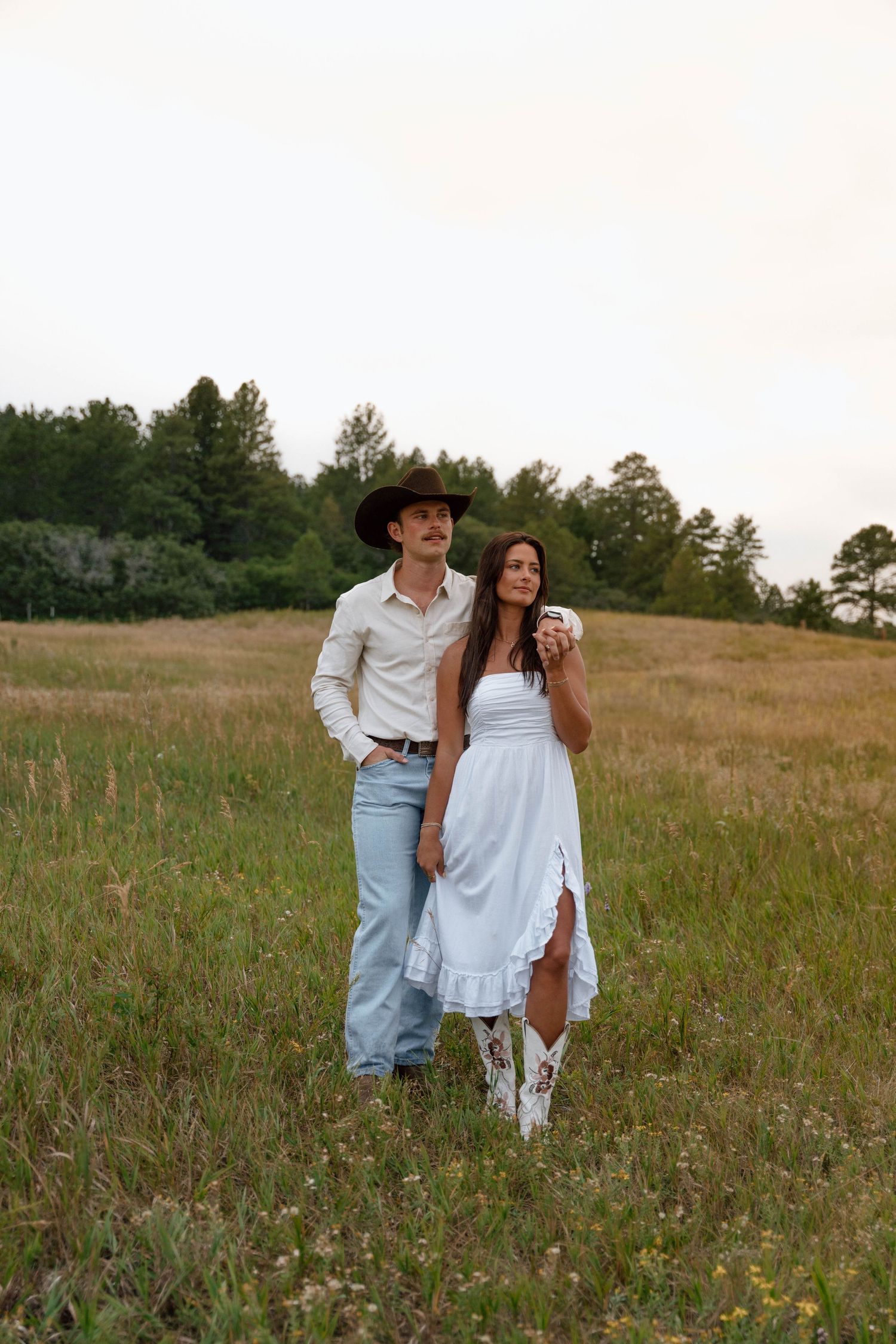 A playful couple shares a laugh while standing in a hilltop meadow.