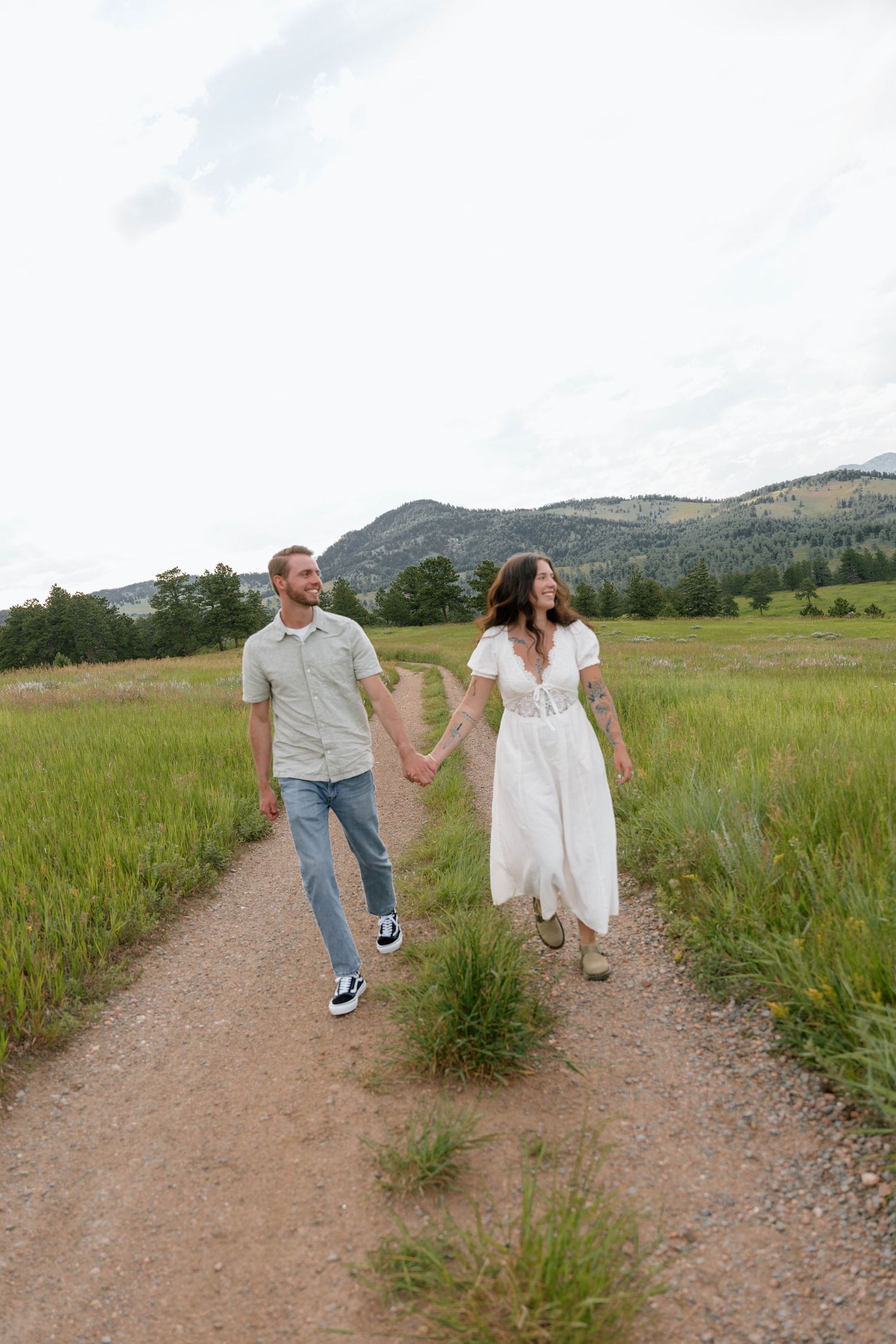 Couple walking hand in hand on mountain trail wearing casual summer attire.