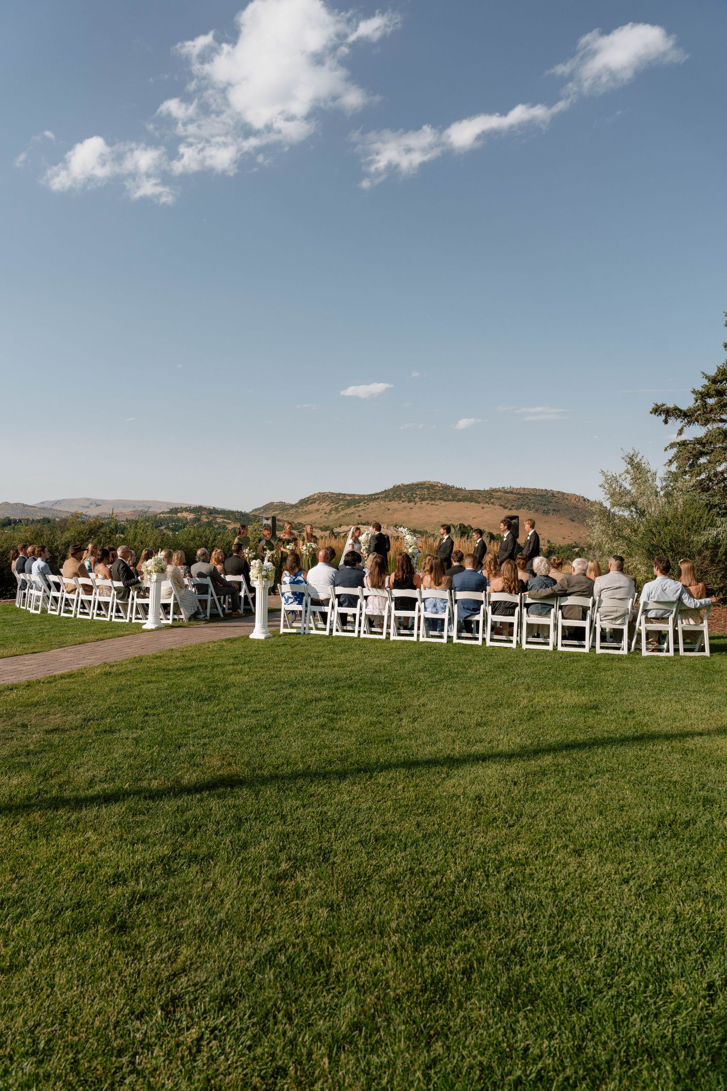 Wedding guests seated on white chairs with mountain views during an outdoor ceremony.