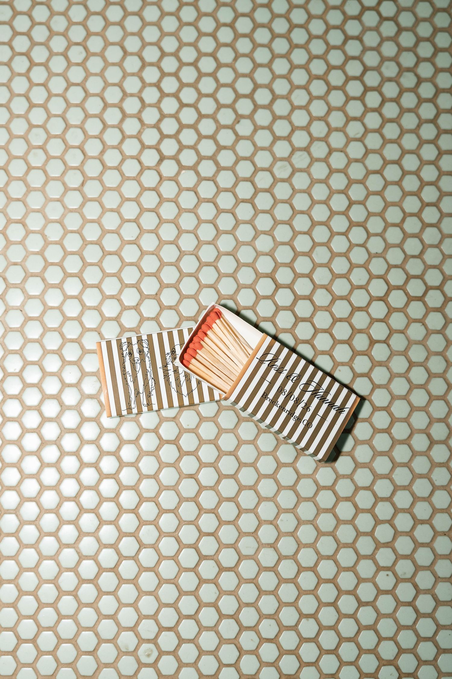 Open matchbox with red-tipped matches on hexagonal tile background.