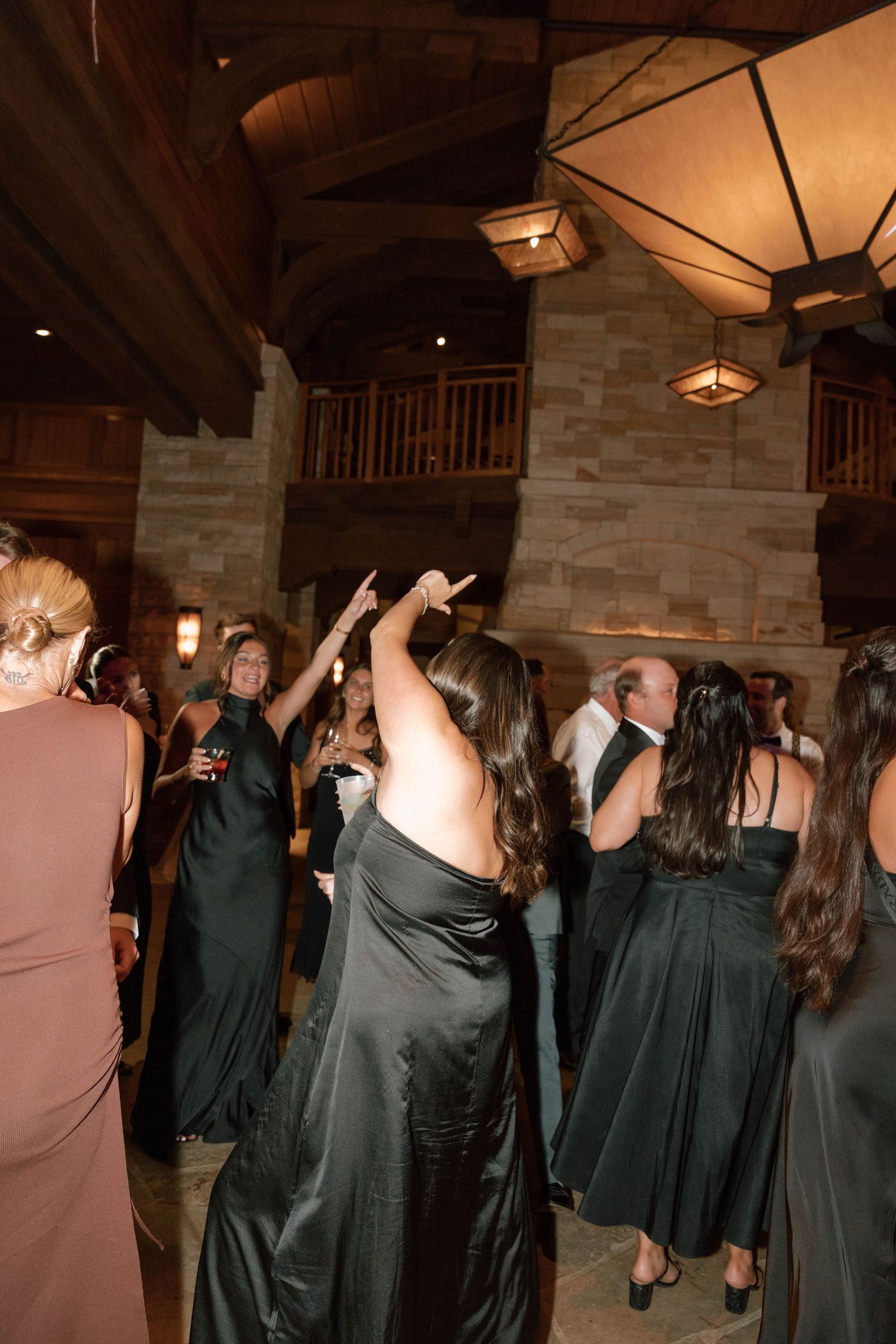 Wedding party members in dark formal attire dance together on the reception floor.