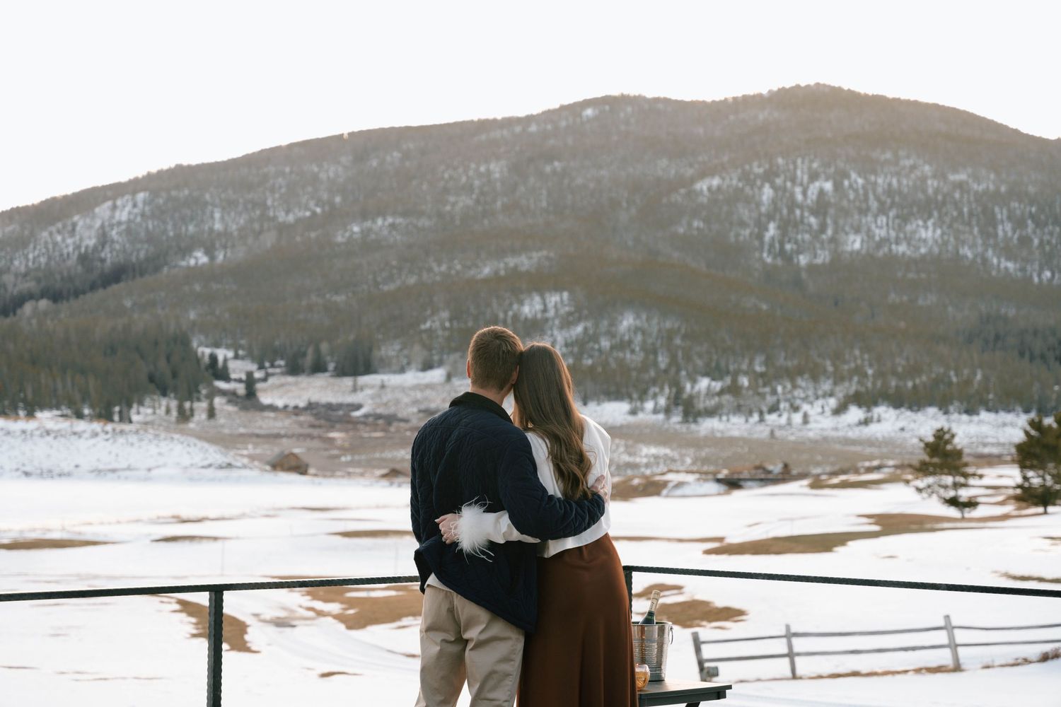 Wide landscape view of a couple on a terrace with snow-capped mountains in the distance.