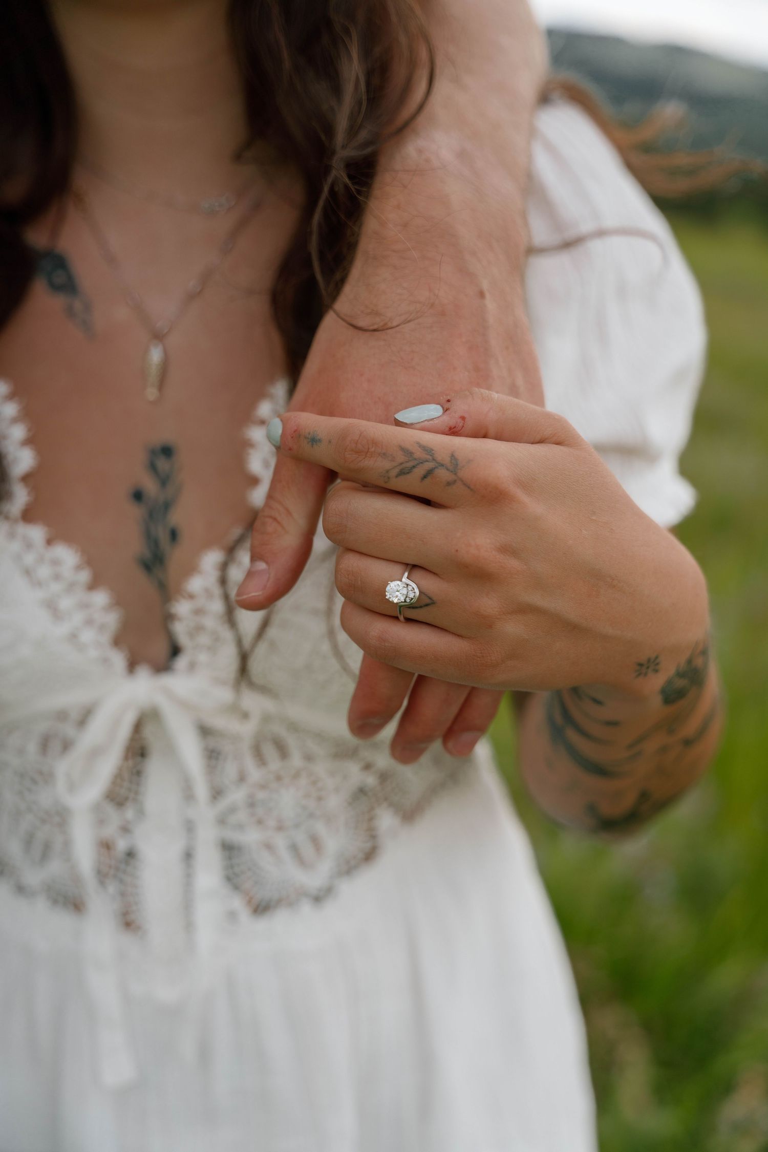 Close-up detail of engagement ring and lace dress in an outdoor meadow setting.