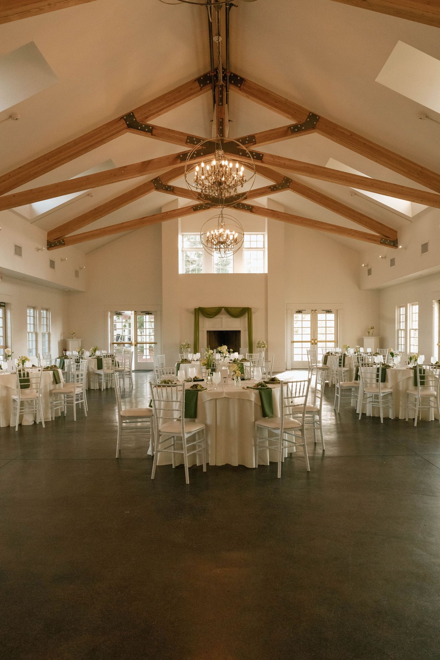 Spacious wedding venue with exposed wooden beams, white walls, and elegant round tables.