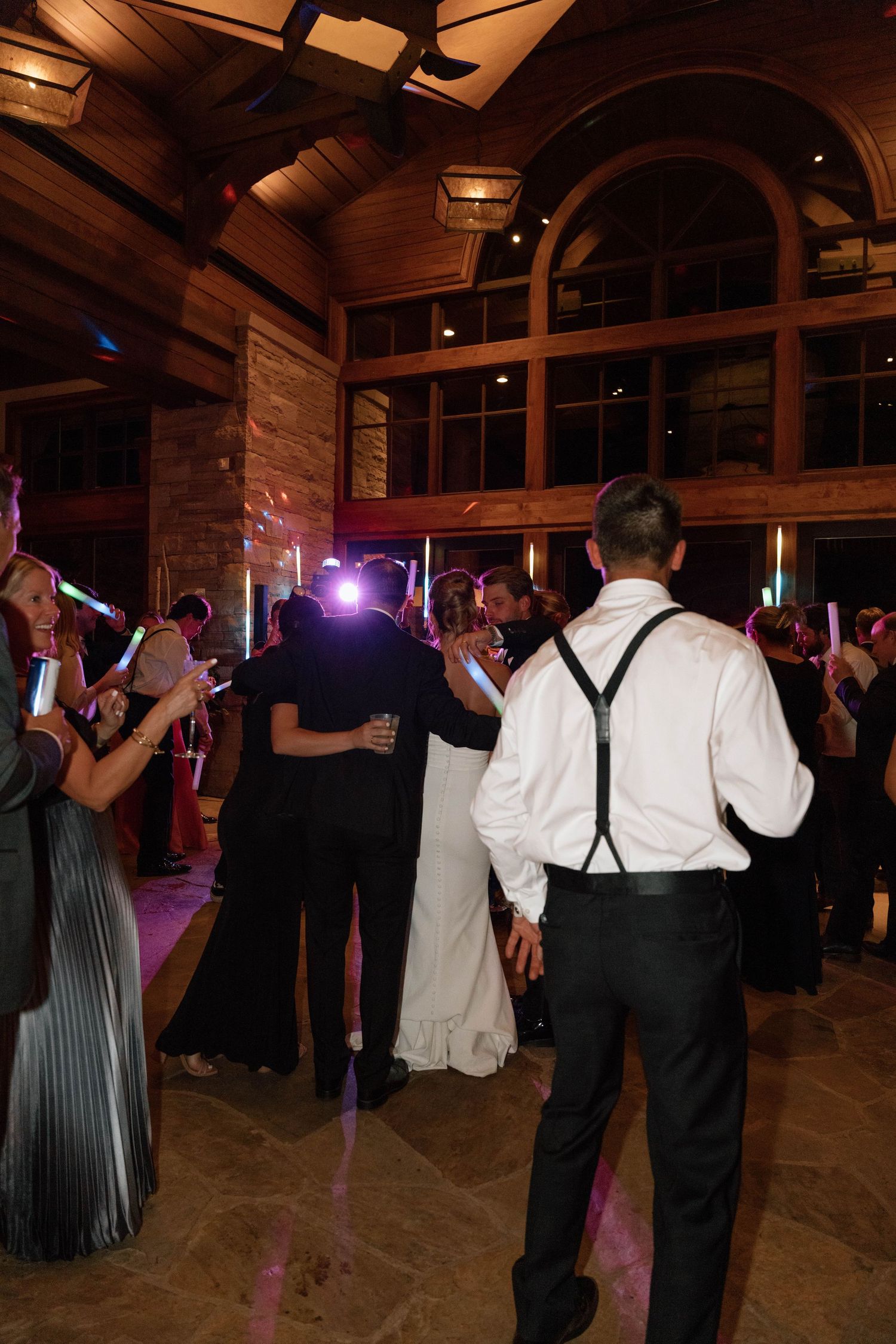 Wedding guests dancing under purple lighting in a rustic reception hall.