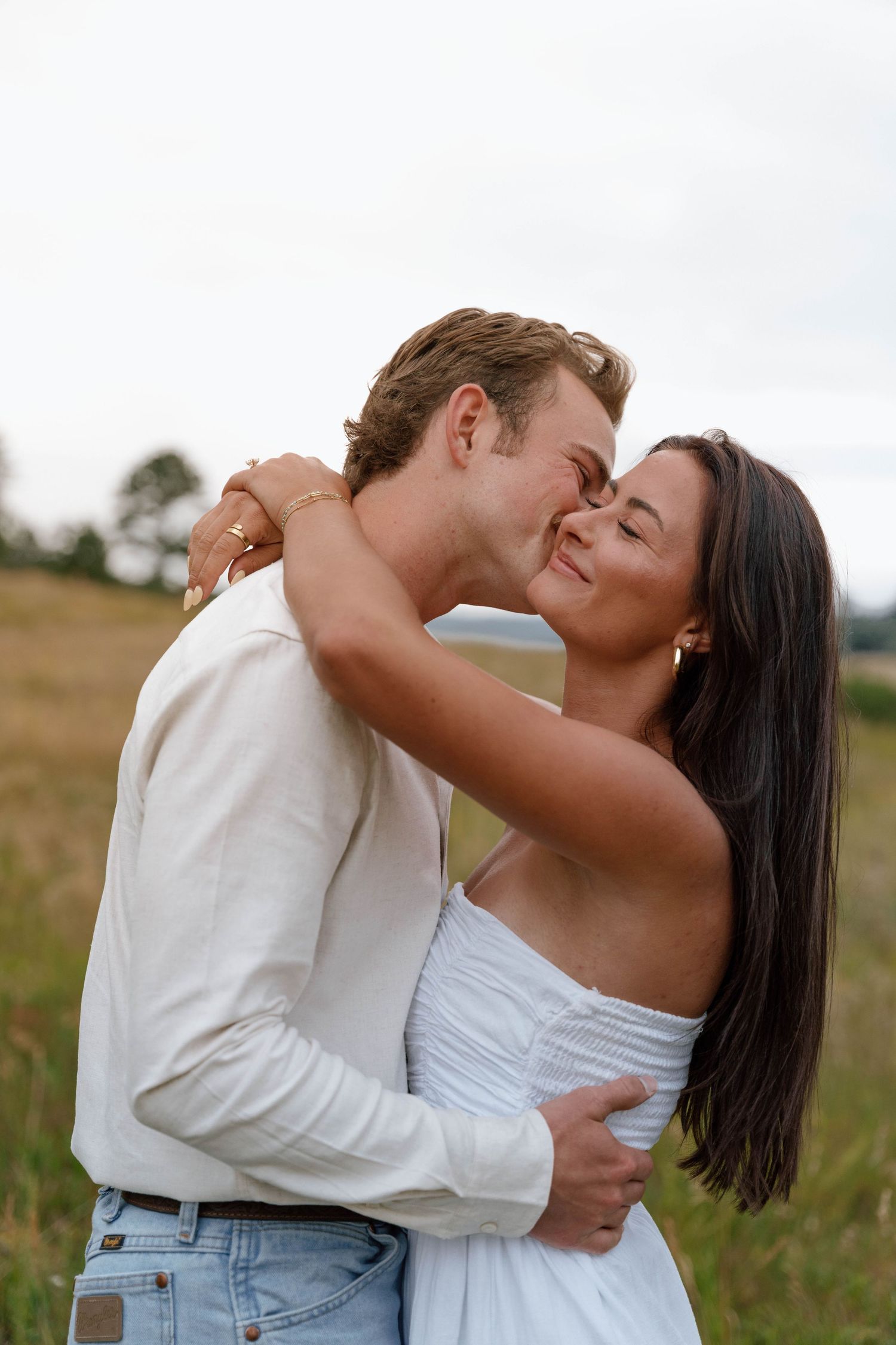 Romantic couple embracing in a sunlit meadow wearing white and denim.