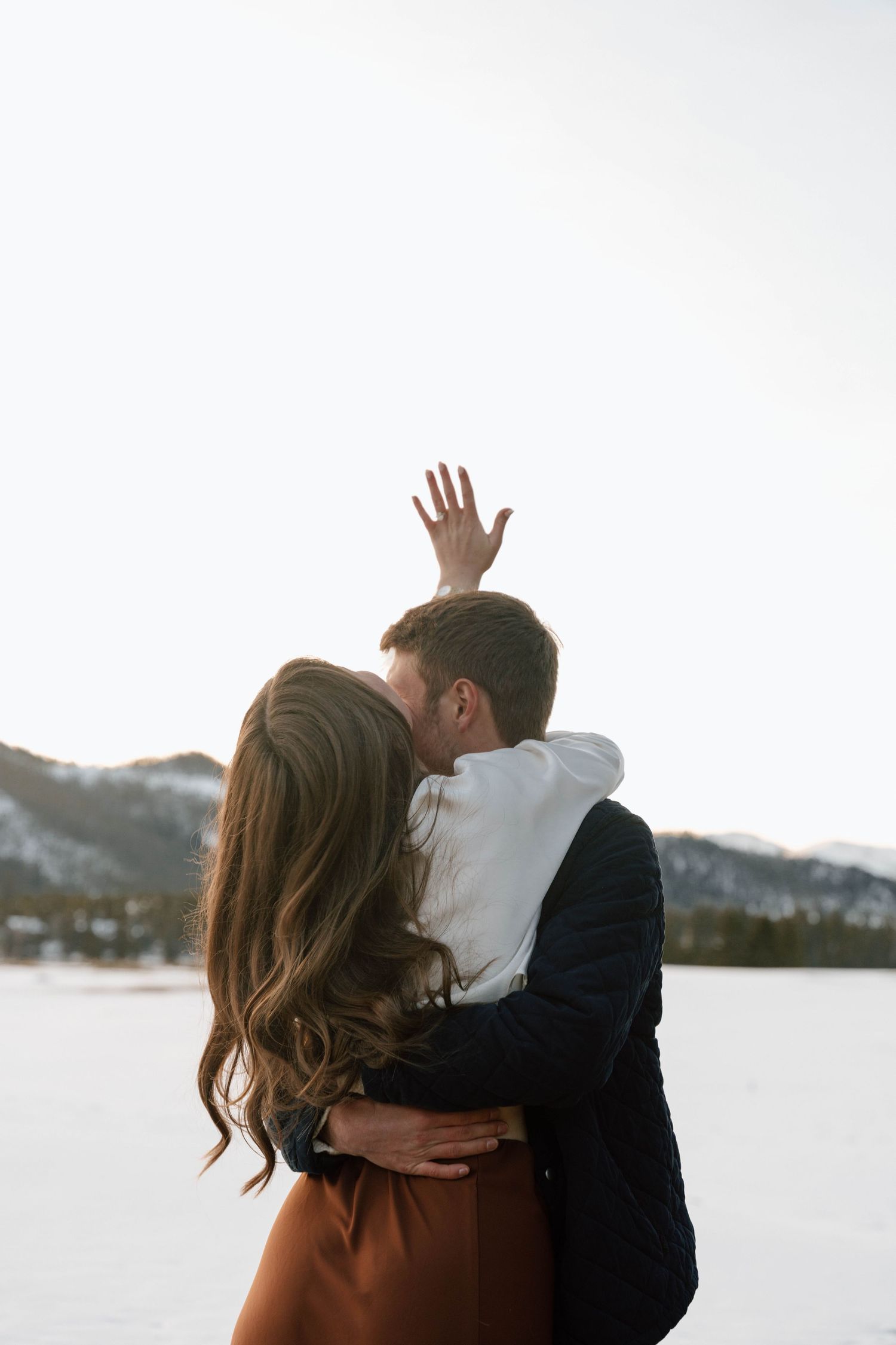 A romantic winter photoshoot by a snowy lake with mountains in the background.