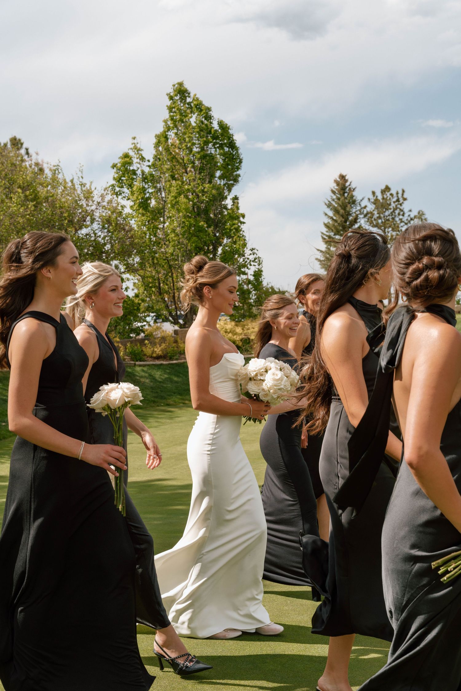 A wedding party walking in formation across a golf course carrying white bouquets.