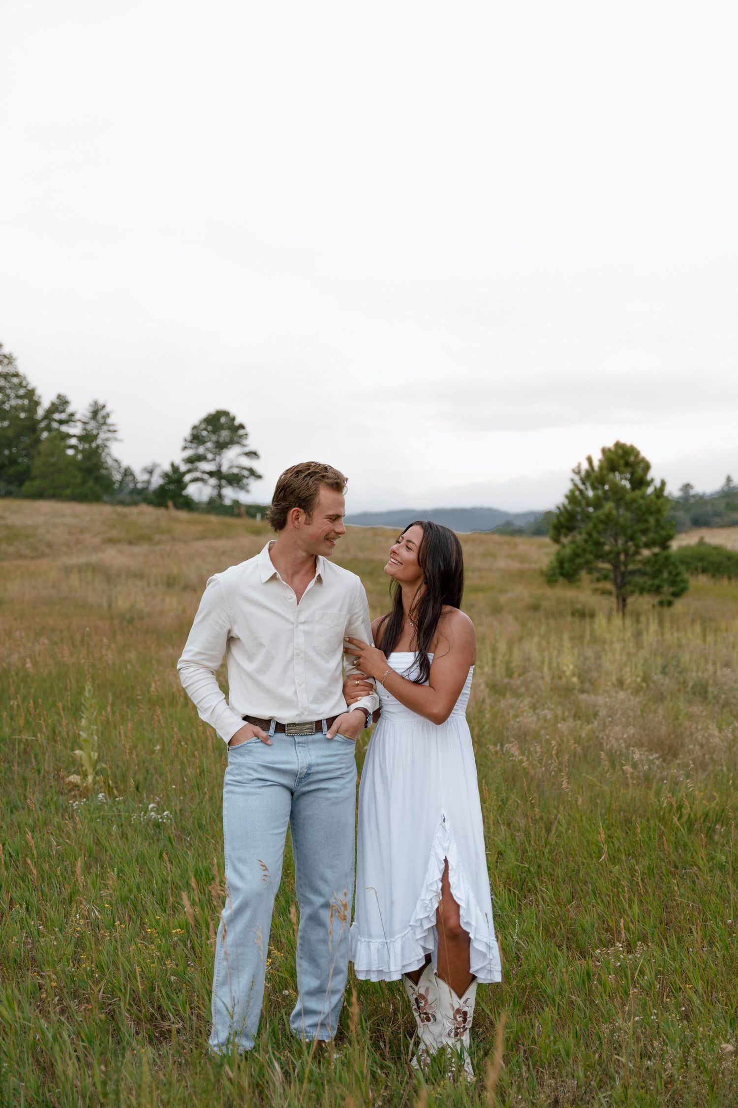 A couple shares a tender moment in a mountain meadow wearing coordinating white outfits.