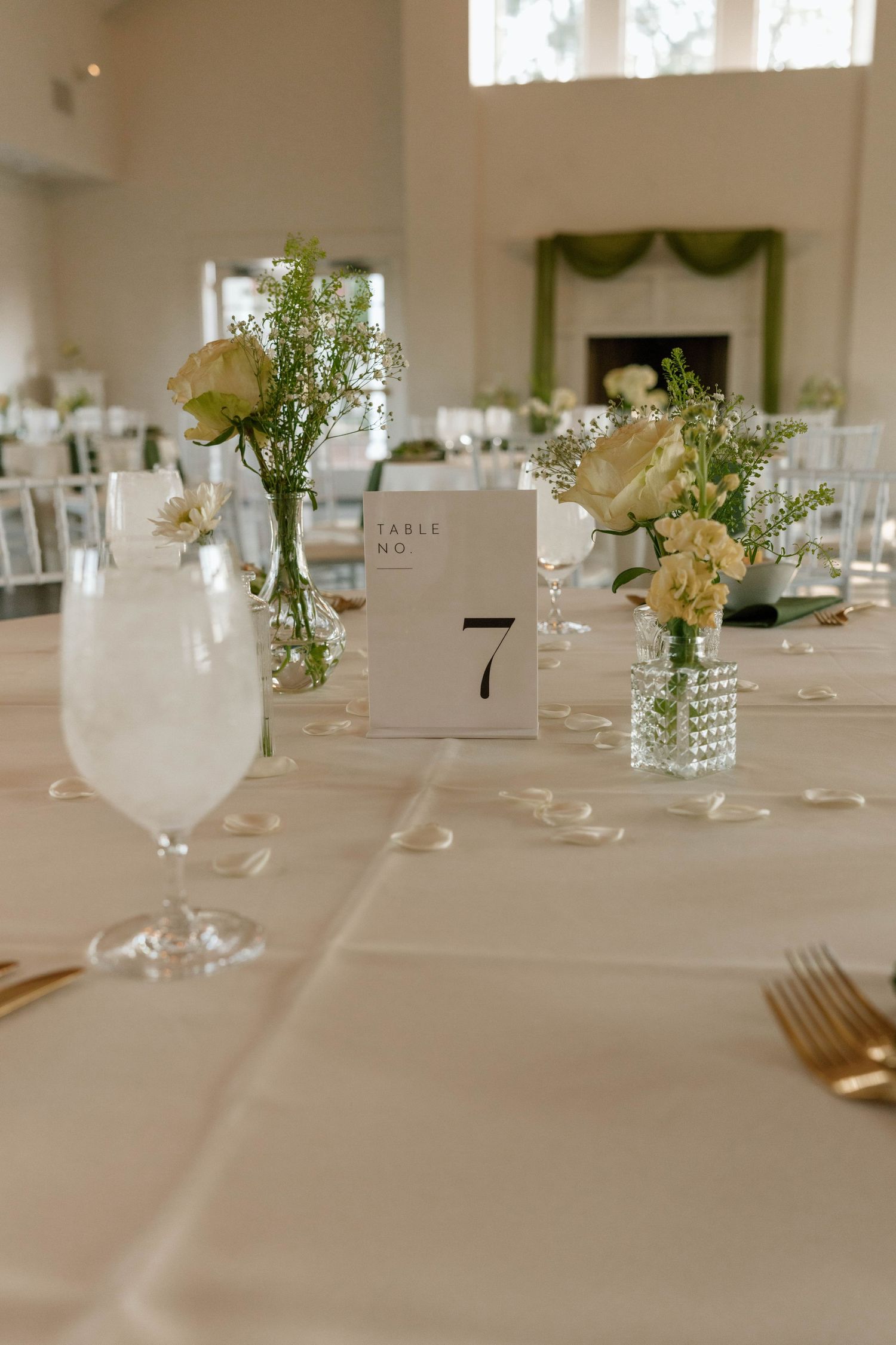 Elegant white table setting with floral centerpieces and table numbers for a wedding reception.