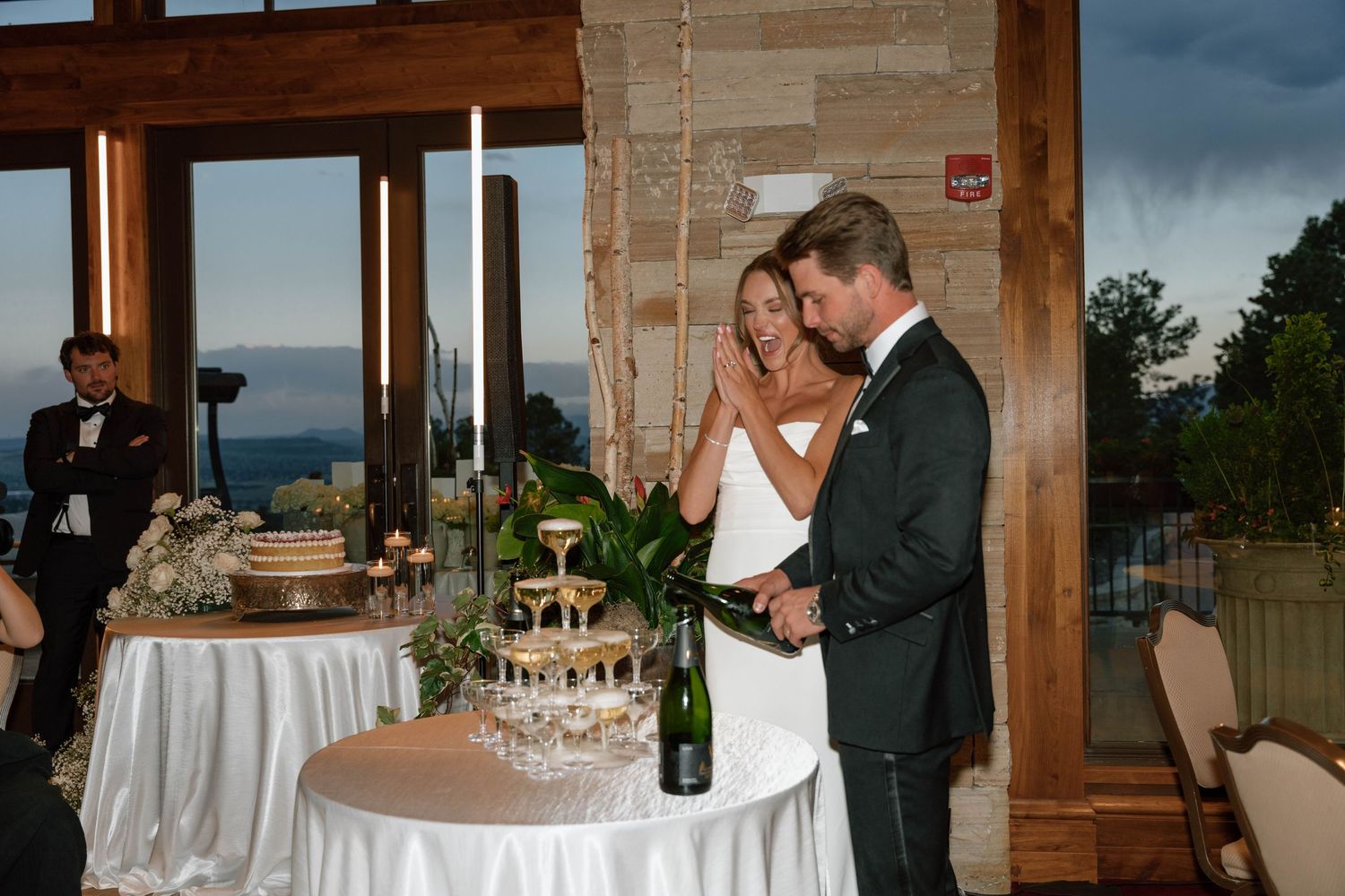 Wedding reception venue with white tablecloths and panoramic windows overlooking scenic views.