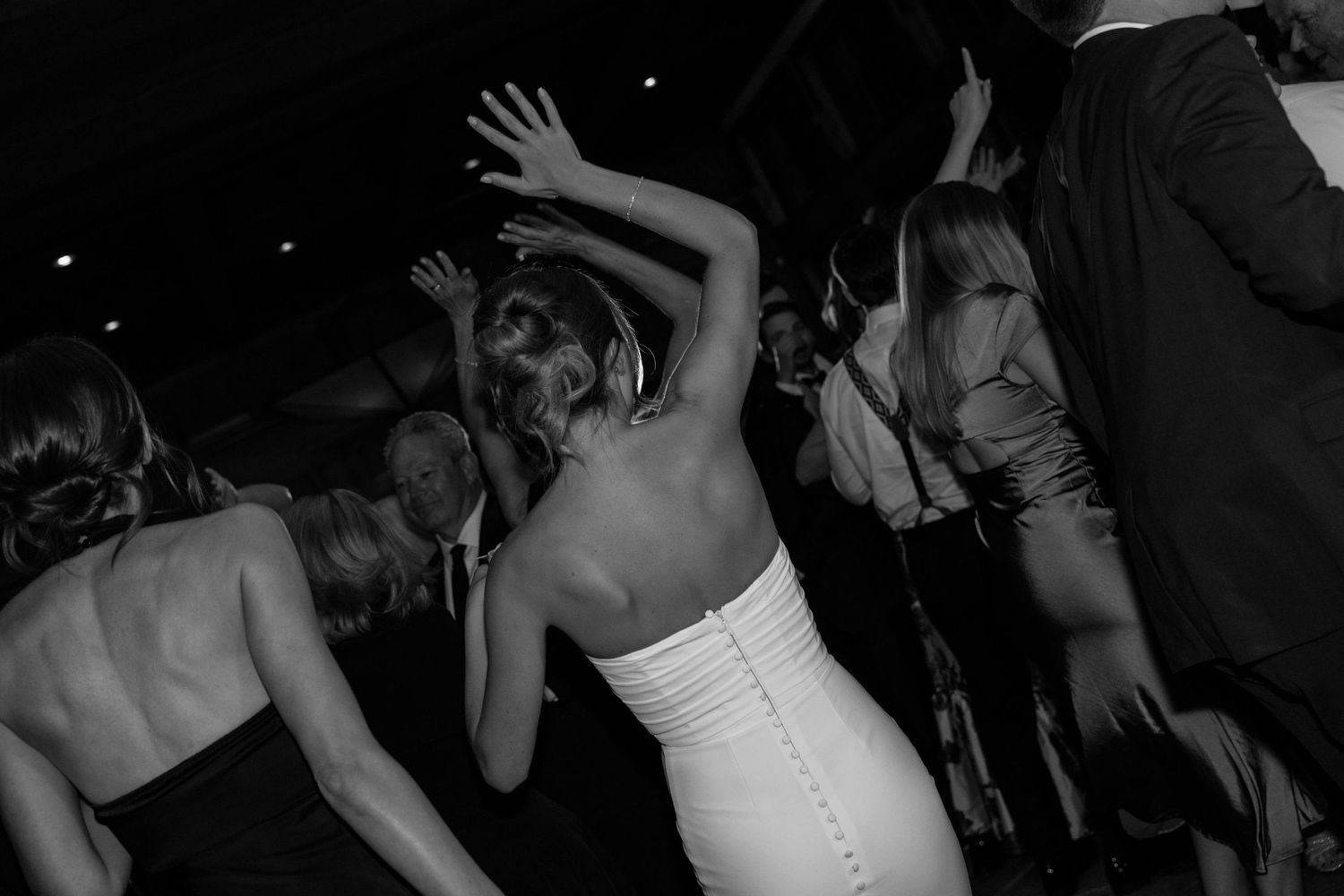 Wedding guests dancing energetically at a dimly lit reception venue.