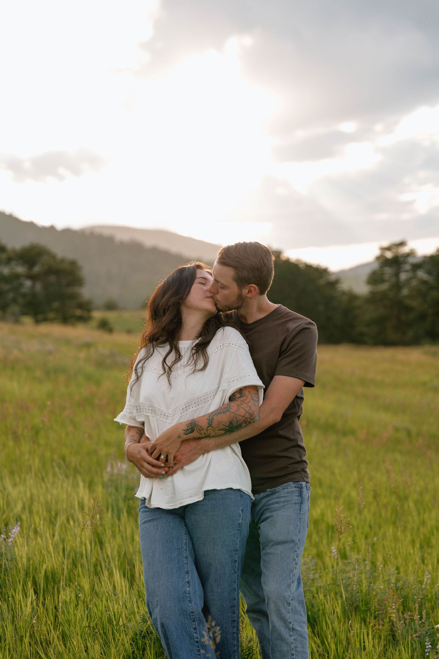 A loving embrace in a mountain meadow at sunset with wildflowers and rolling hills.