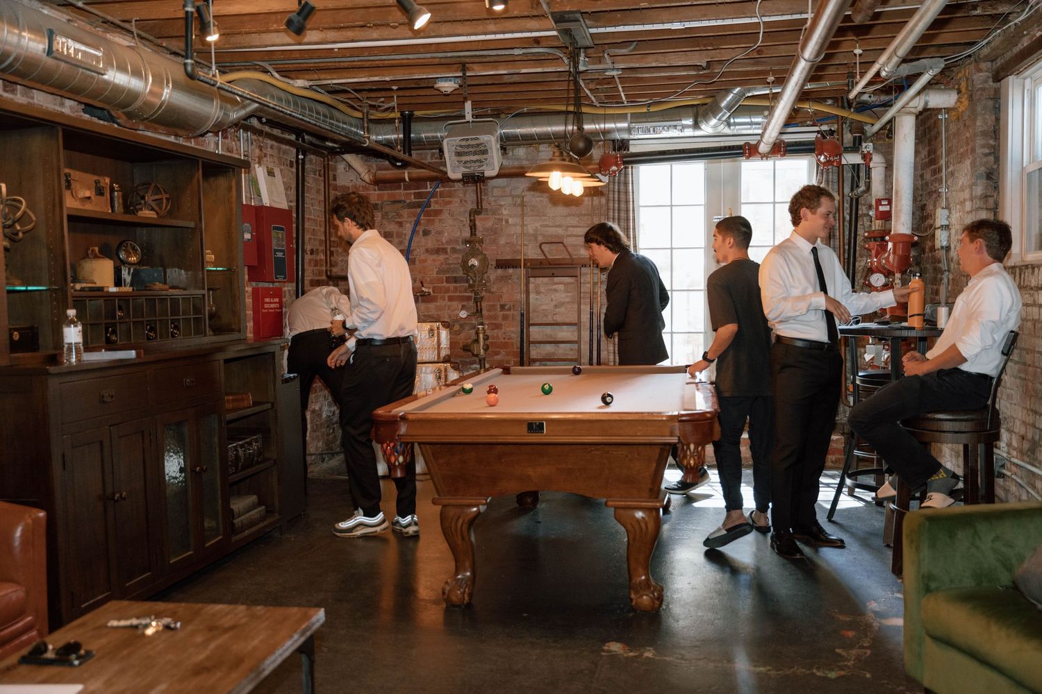 People gather in an industrial-style basement venue with exposed brick walls and wooden furniture.