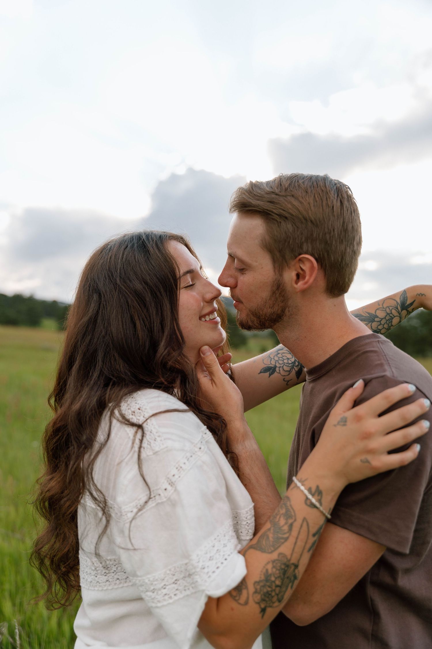 An intimate moment between a couple in a summer meadow with soft clouds in the background.