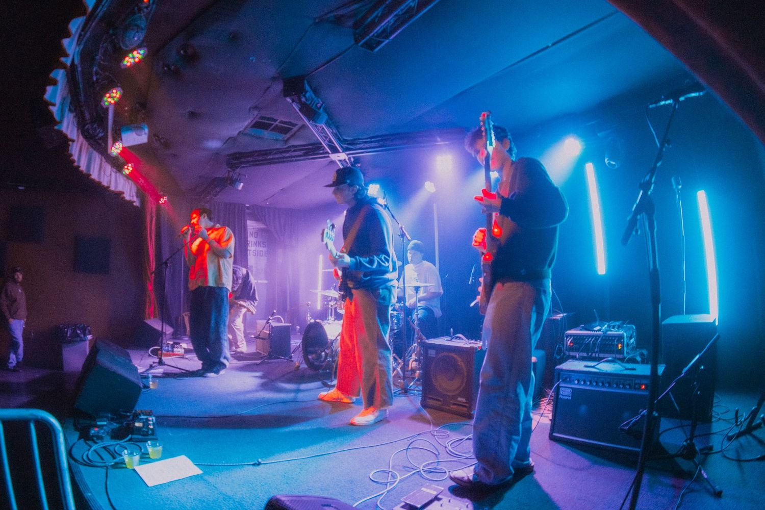 Musicians perform on stage with dramatic blue lighting and fog effects during a live concert performance.