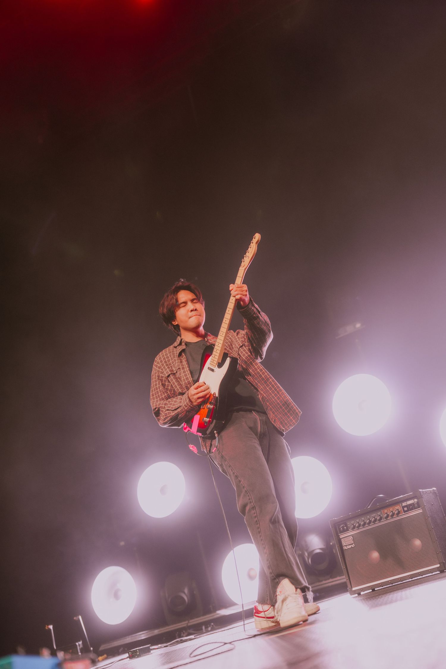 Concert performer silhouetted against dramatic red stage lighting while playing guitar during live show.